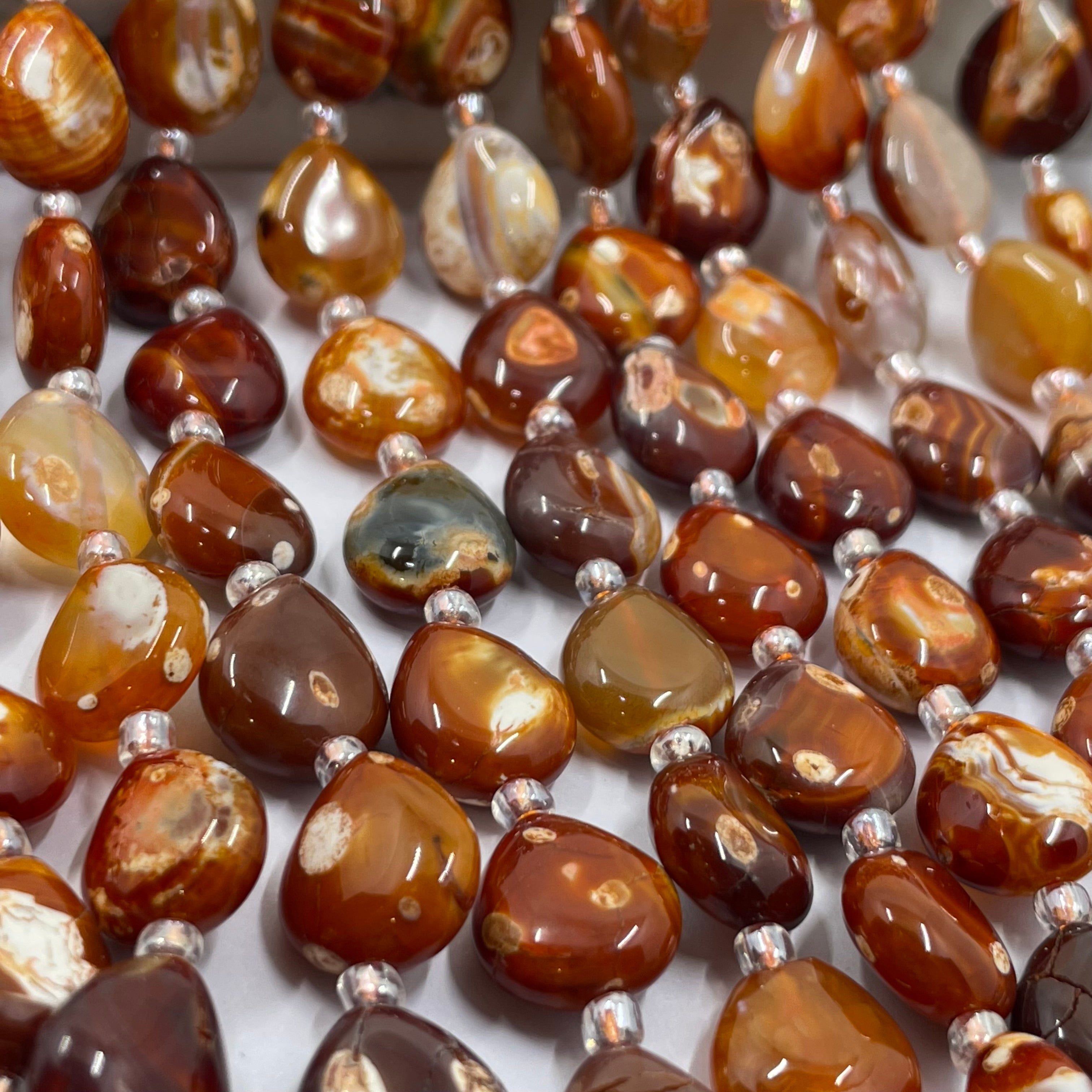 Close-up of polished brown terracotta stone beads strung on silver cord, showing natural marbled patterns in amber, caramel, and dark brown tones.