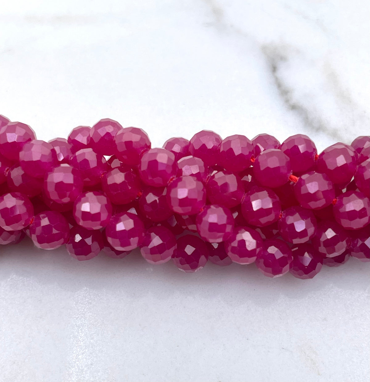 A close-up of faceted magenta pink ruby beads strung together on a white marble surface.