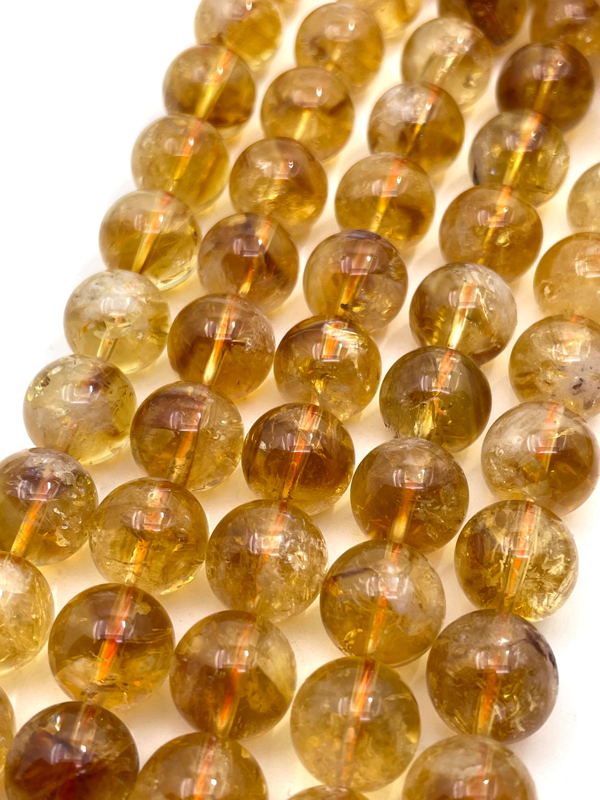 A close-up of multiple strands of round, translucent amber-yellow citrine beads on a white background.