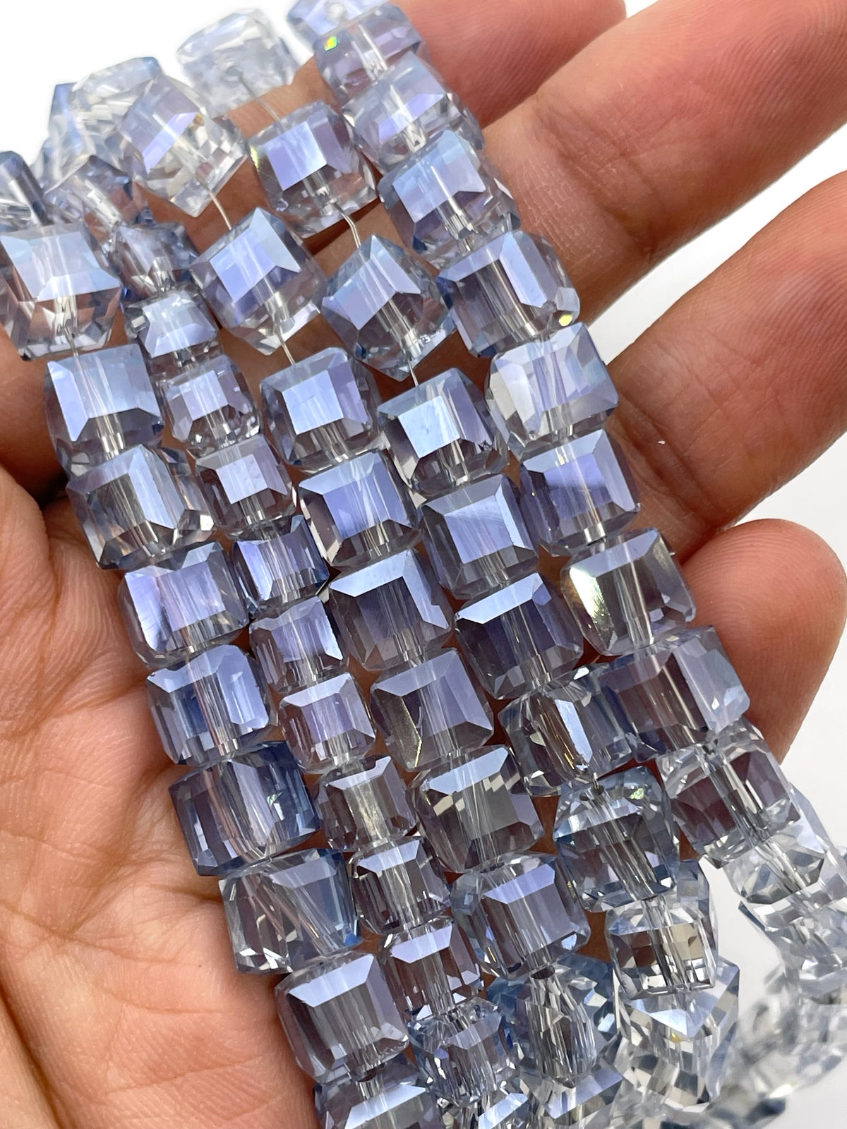 A close-up of a hand holding multiple strands of faceted cube beads with a light blue-gray iridescent finish.