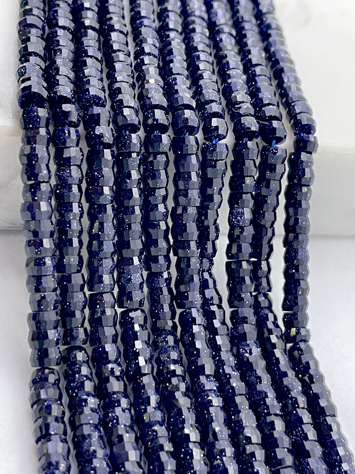 Multiple strands of faceted dark blue sandstone with embedded glitter, arranged vertically on a white background.