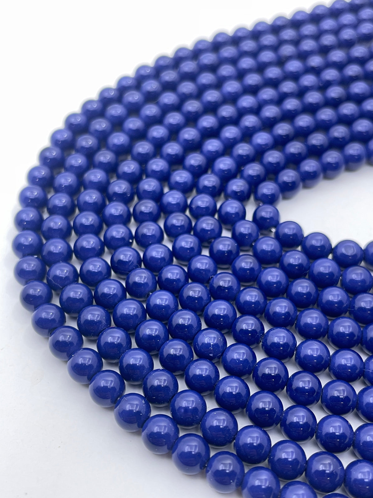 Multiple strands of polished, round cobalt blue shell pearls arranged in a curved pattern on a plain white background.