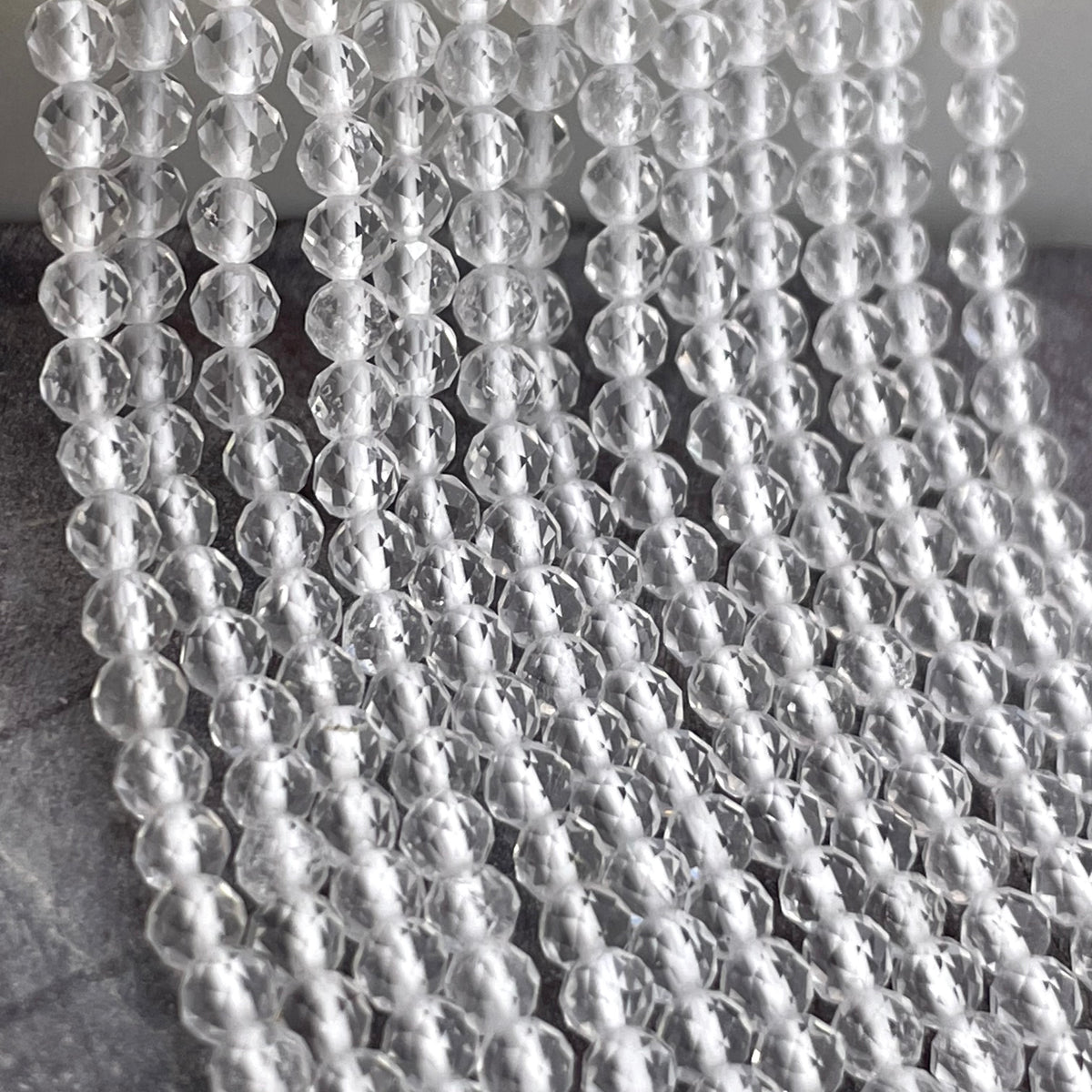 Clear faceted glass beads strung in multiple parallel rows, photographed close-up against a neutral gray background.