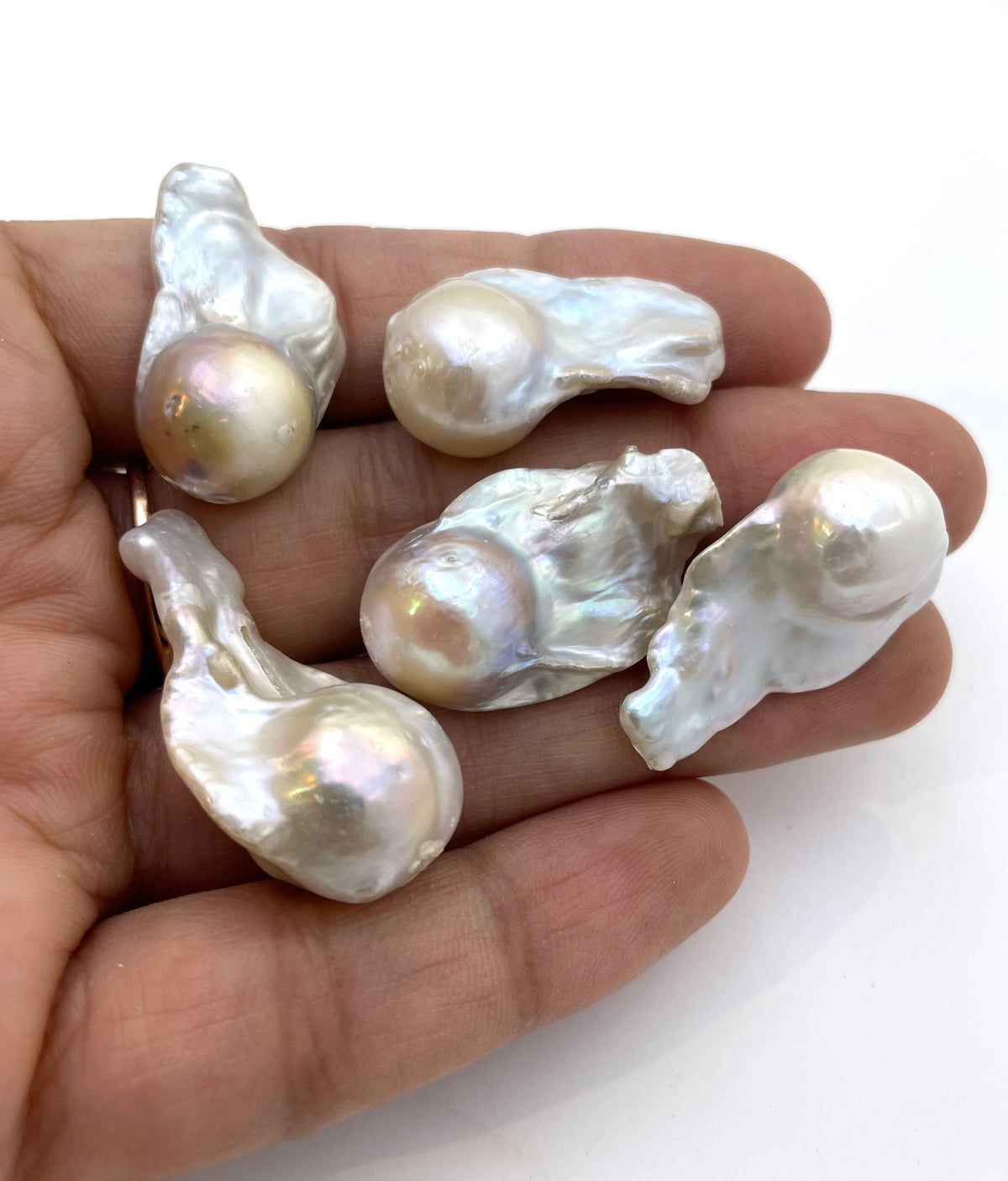 Five irregular baroque pearls displayed on a person's hand against a plain white background.