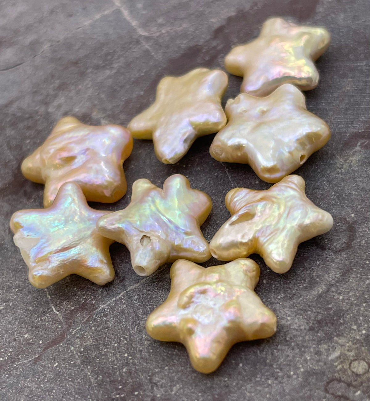 Seven star-shaped baroque pearls with an iridescent finish, scattered on a dark gray slate surface.