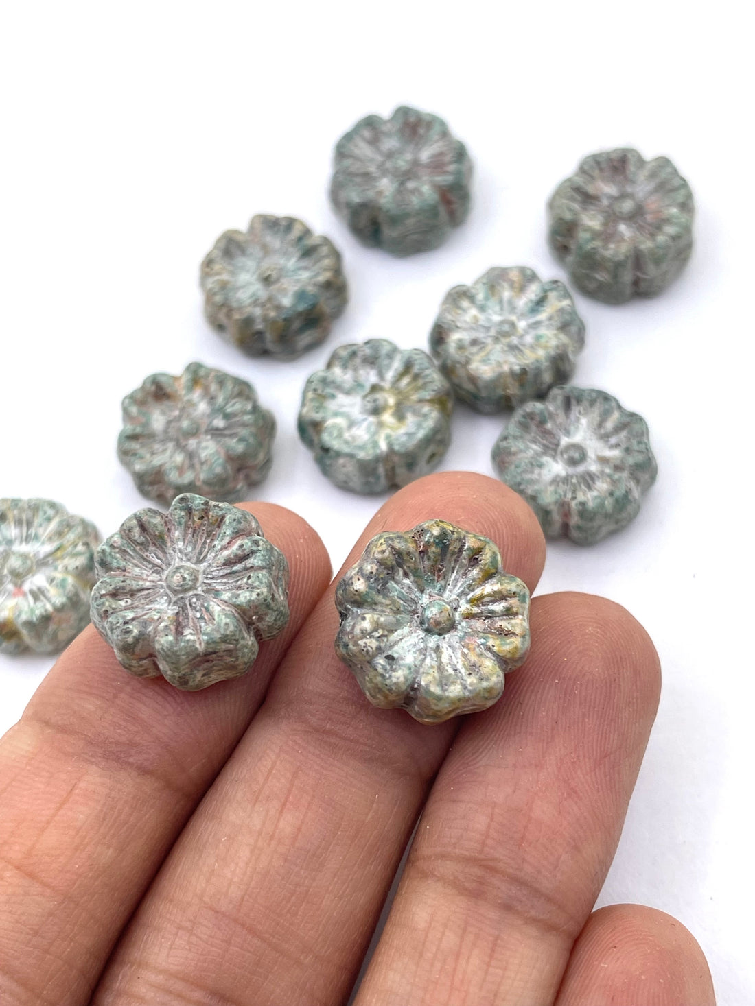 A group of small, textured, flower-shaped beads in a mottled green and gray stone-like finish, arranged on a plain white background.