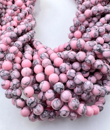 Multiple strands of round pink howlite gemstone beads with black and gray marbled veining, arranged in a layered display on a white background.