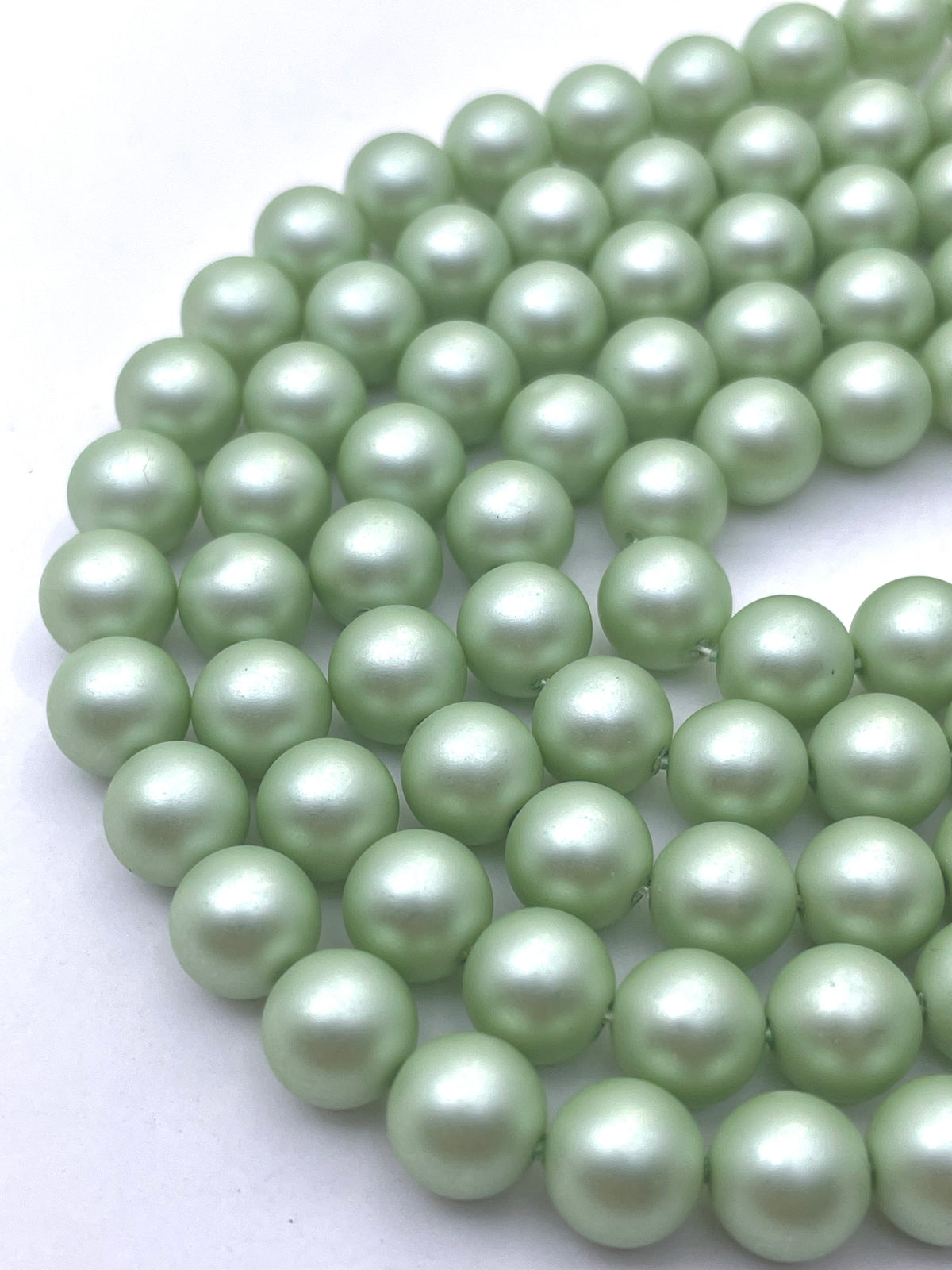 A close-up of pale mint green shell pearl beads arranged in a curved row on a plain white background.