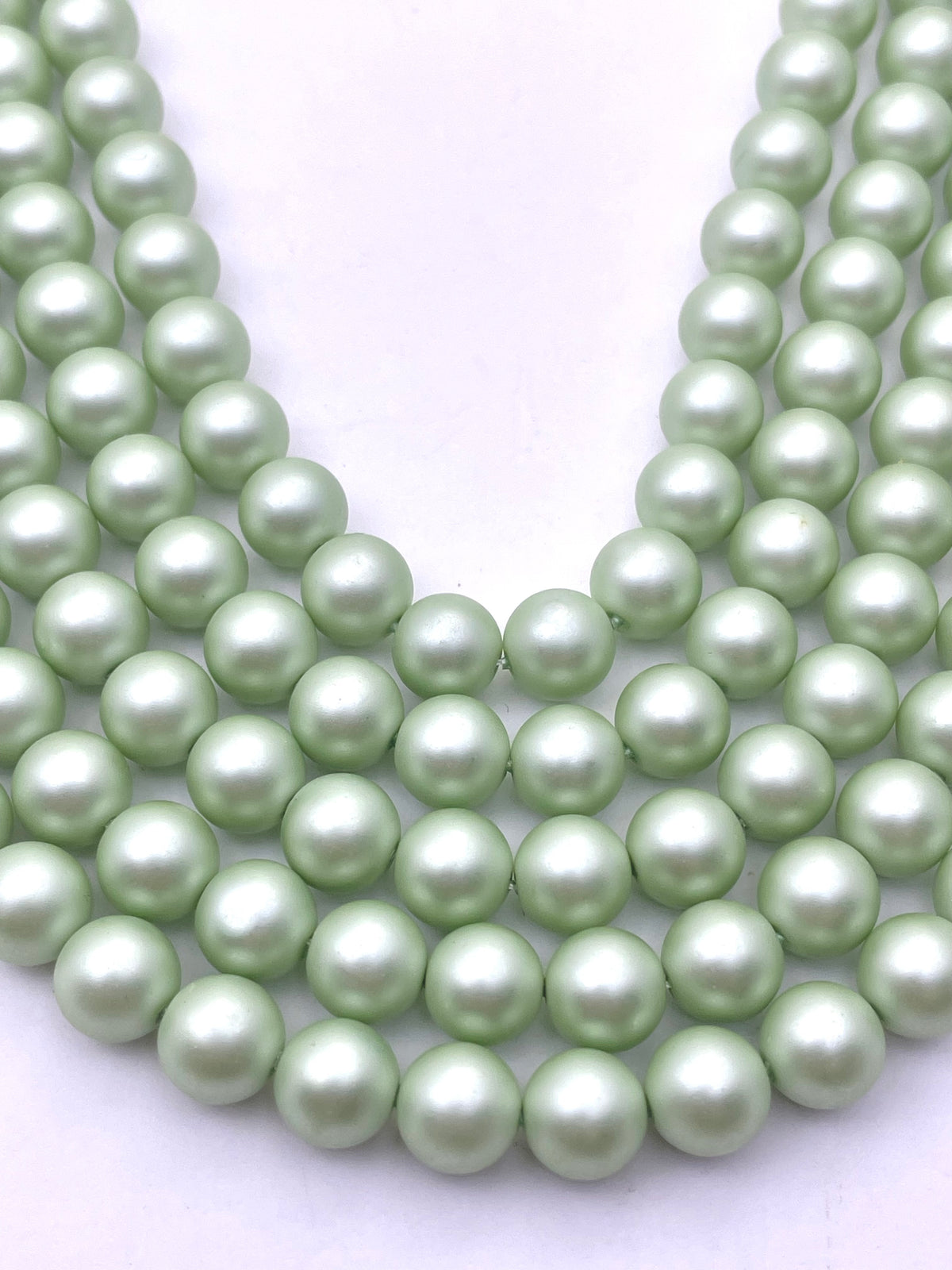 A close-up of multiple strands of light green shell pearl beads arranged in a U-shape on a plain white background.