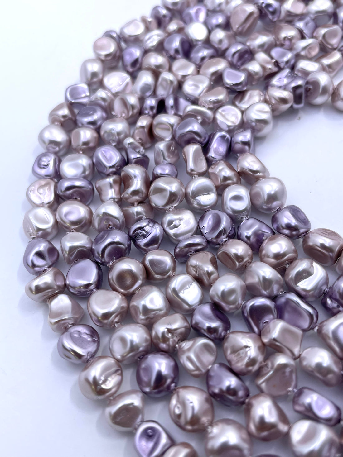 Curled strands of irregular shell pearls in a metallic lavender-gray color, displayed on a clean white background.