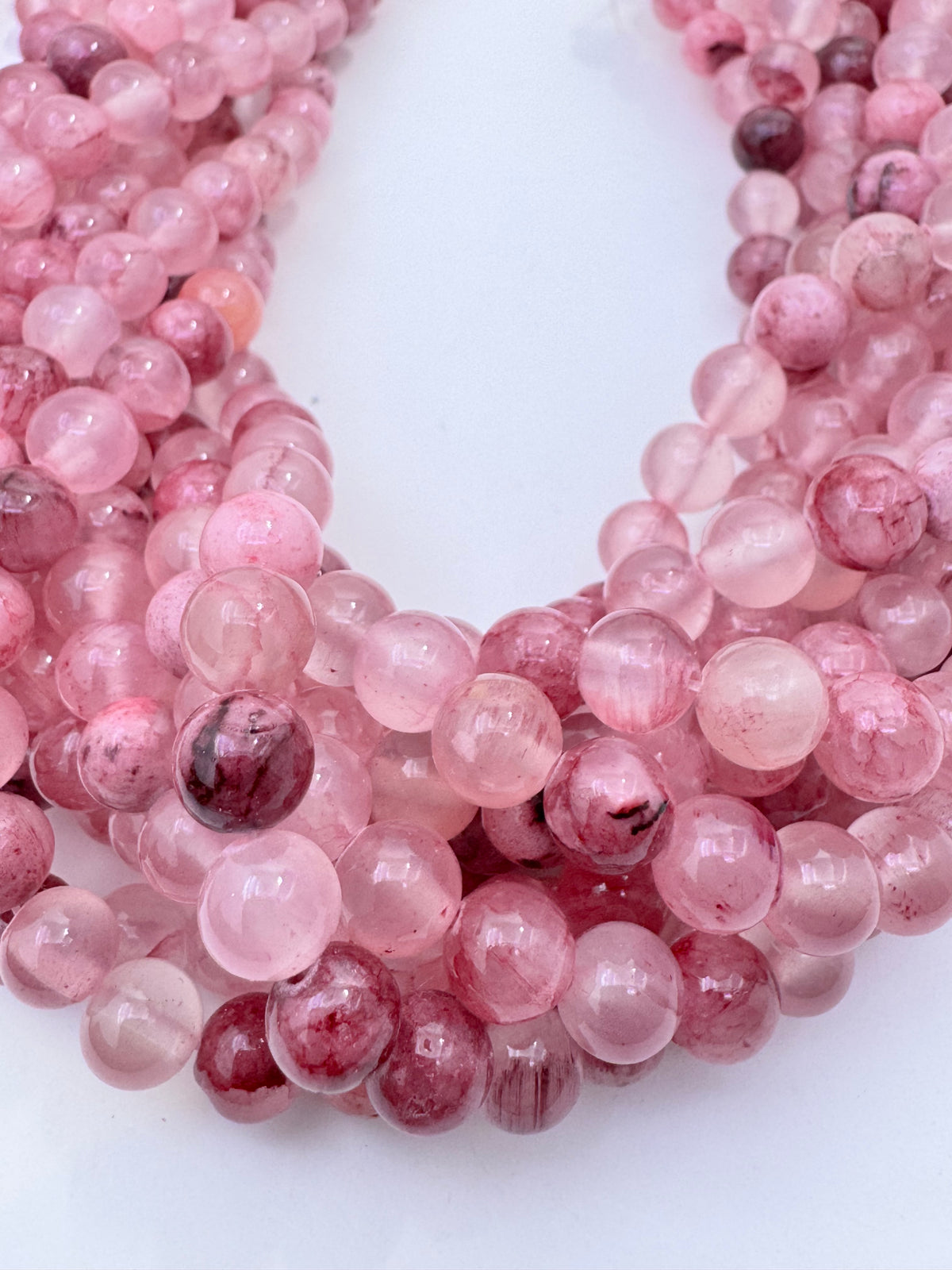 A close-up of multiple strands of round pink persian jade gemstone beads, arranged on a plain white background.