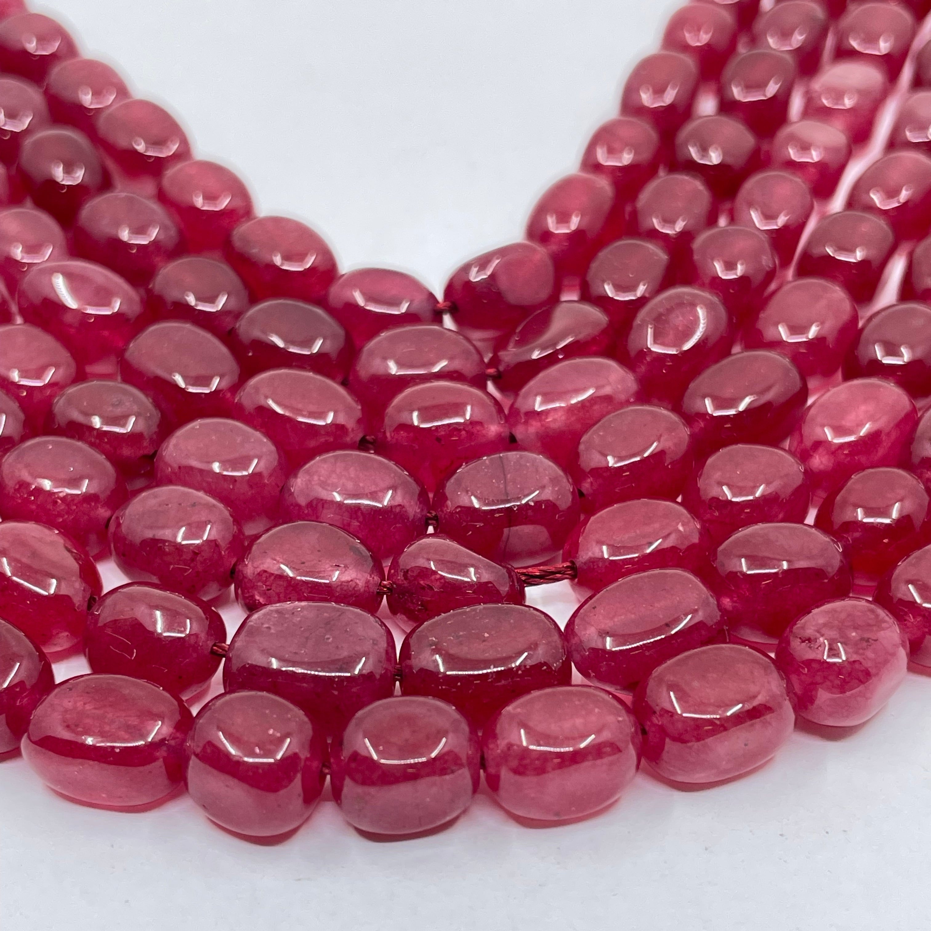 Multiple strands of faceted oval jade beads in a translucent deep pinkish-red color, arranged in a curve on a plain white background.