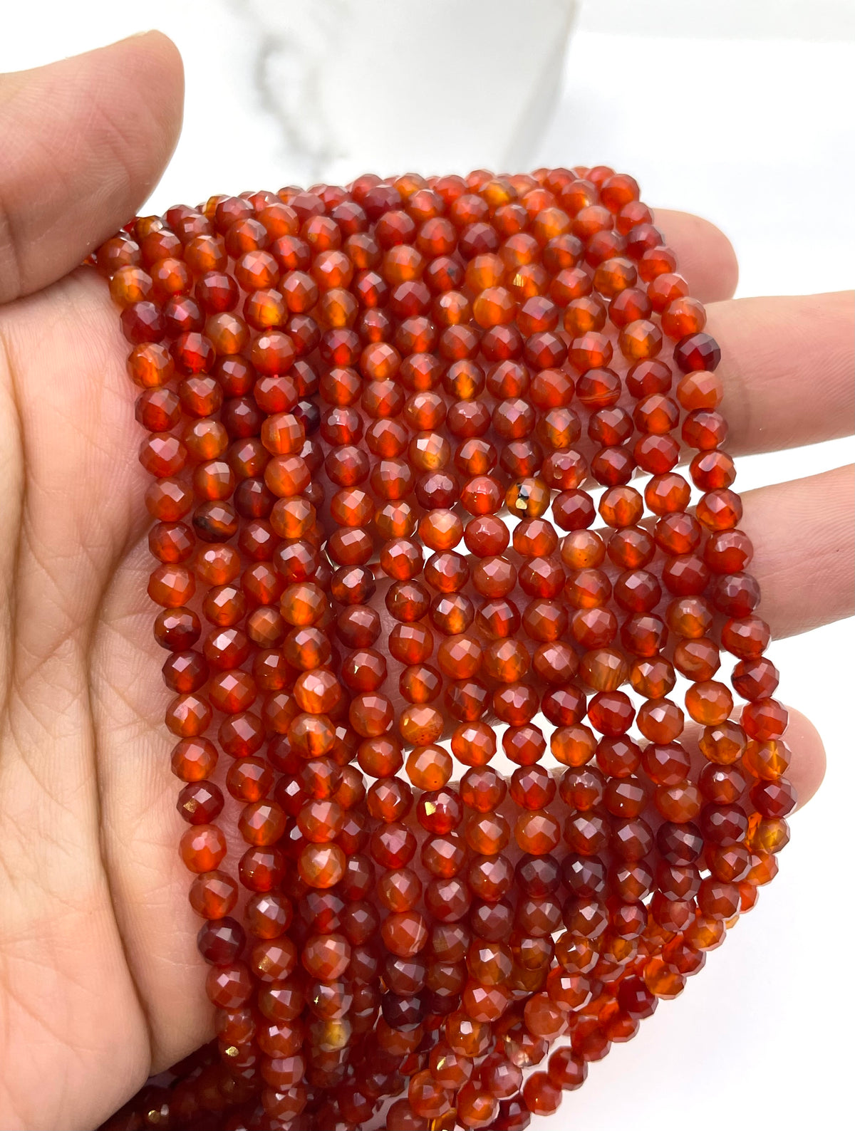 A hand holding a bundle of faceted carnelian beads in multiple strands, showing their warm reddish-brown color and polished round shapes.
