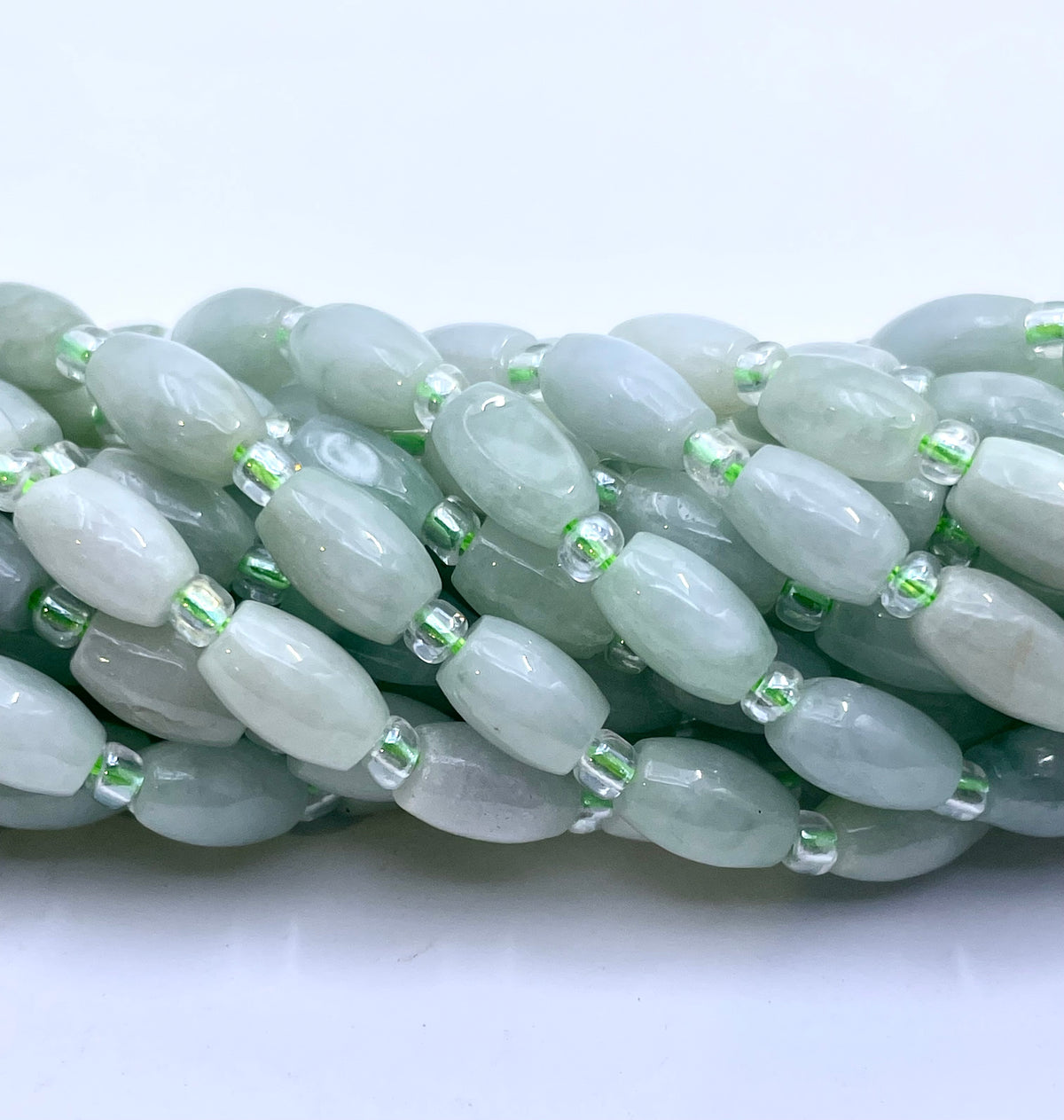Multiple strands of light green burma jade oval beads separated by small clear spacer beads, arranged on a white surface.