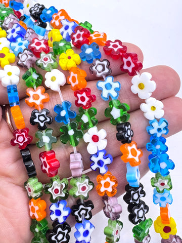 A hand holding several strands of colorful flower-shaped beads on a white background.