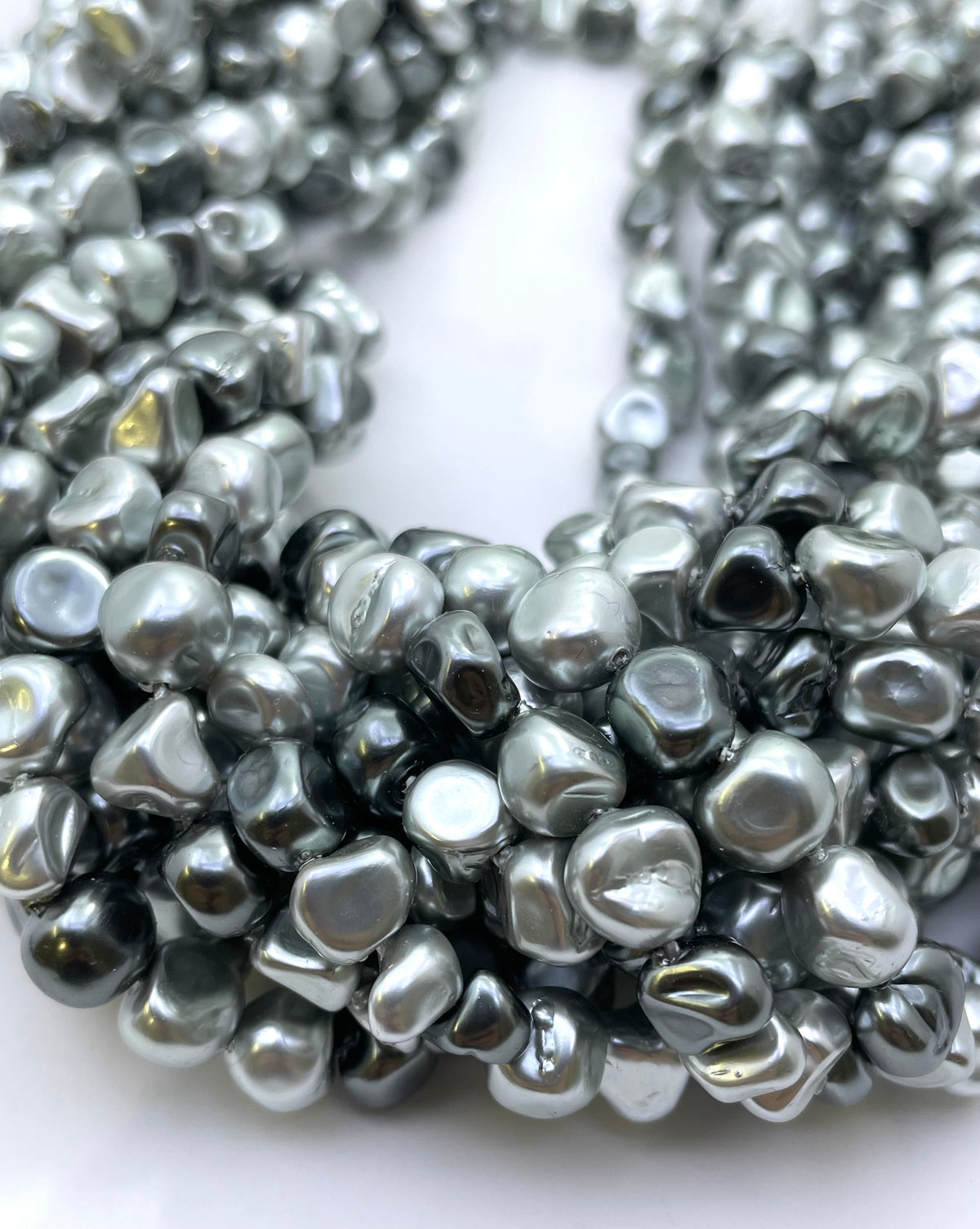 Close-up of a strand of irregular, metallic silver or grey shell pearl beads on a plain white background.