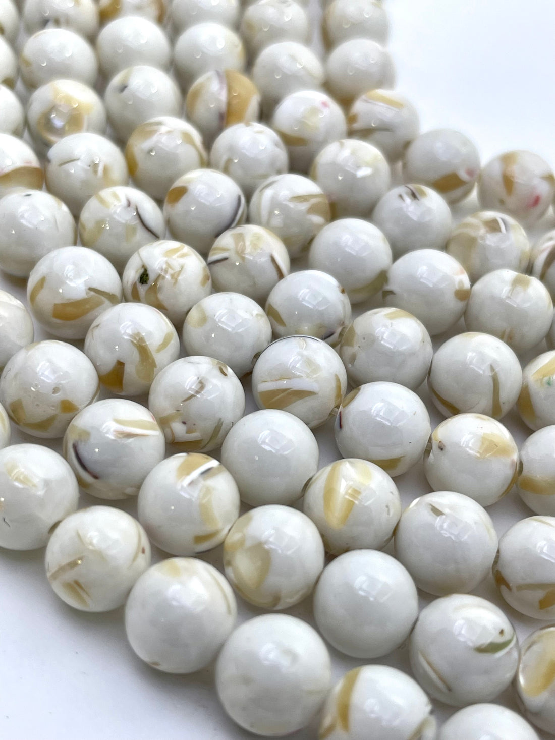 Ivory round mop beads with natural tan and brown inclusions, arranged in diagonal rows on a white background.