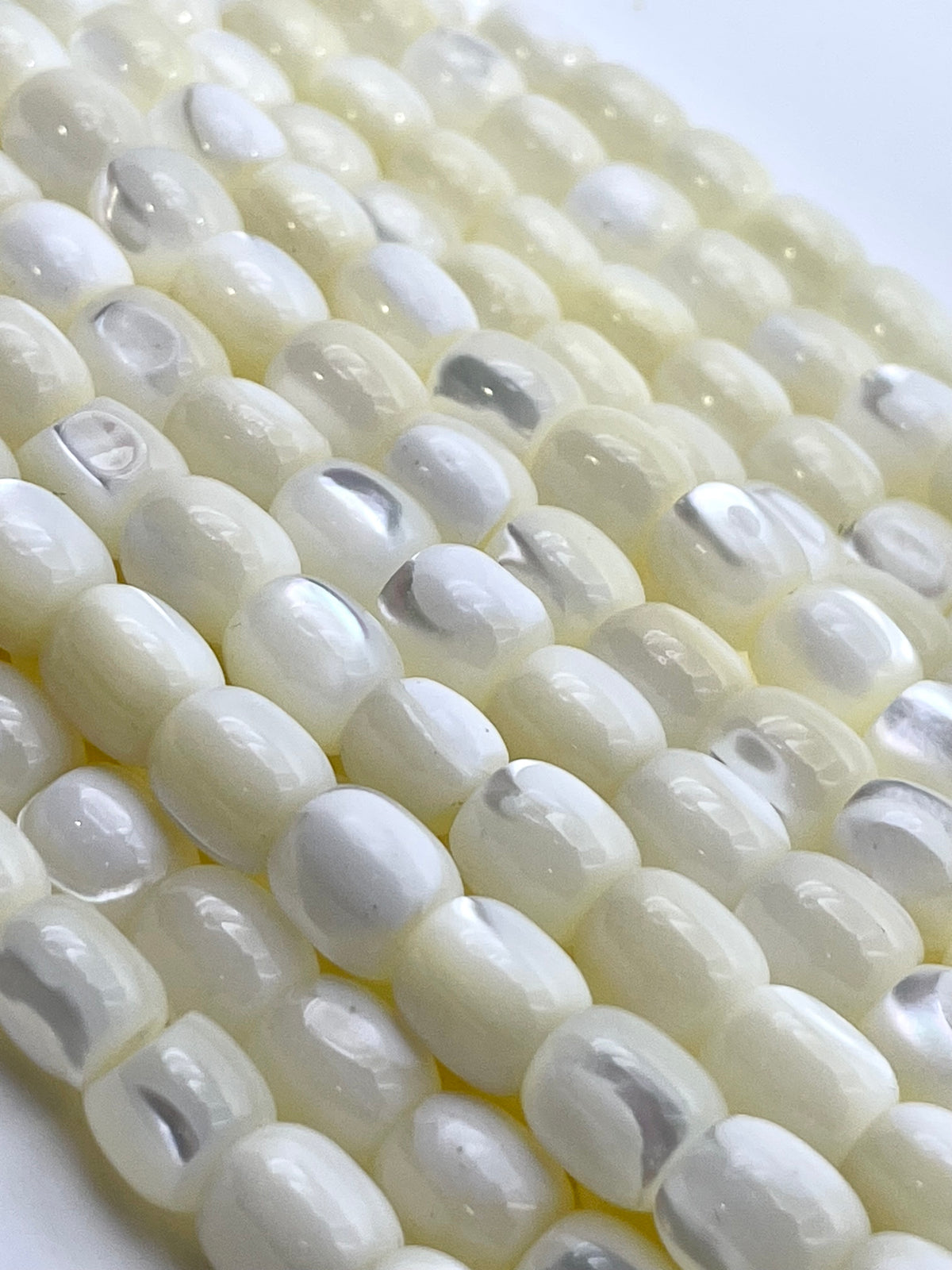 Close-up of multiple strands of glossy, rounded white beads with a subtle pearlescent sheen, arranged diagonally on a light background.