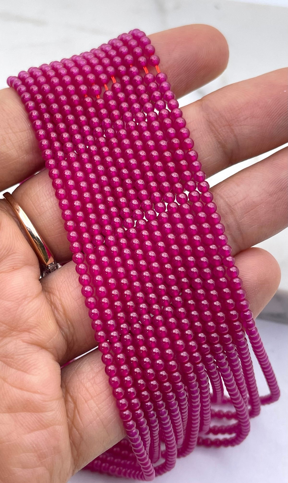 A close-up of a hand holding many parallel strands of small magenta ruby beads.