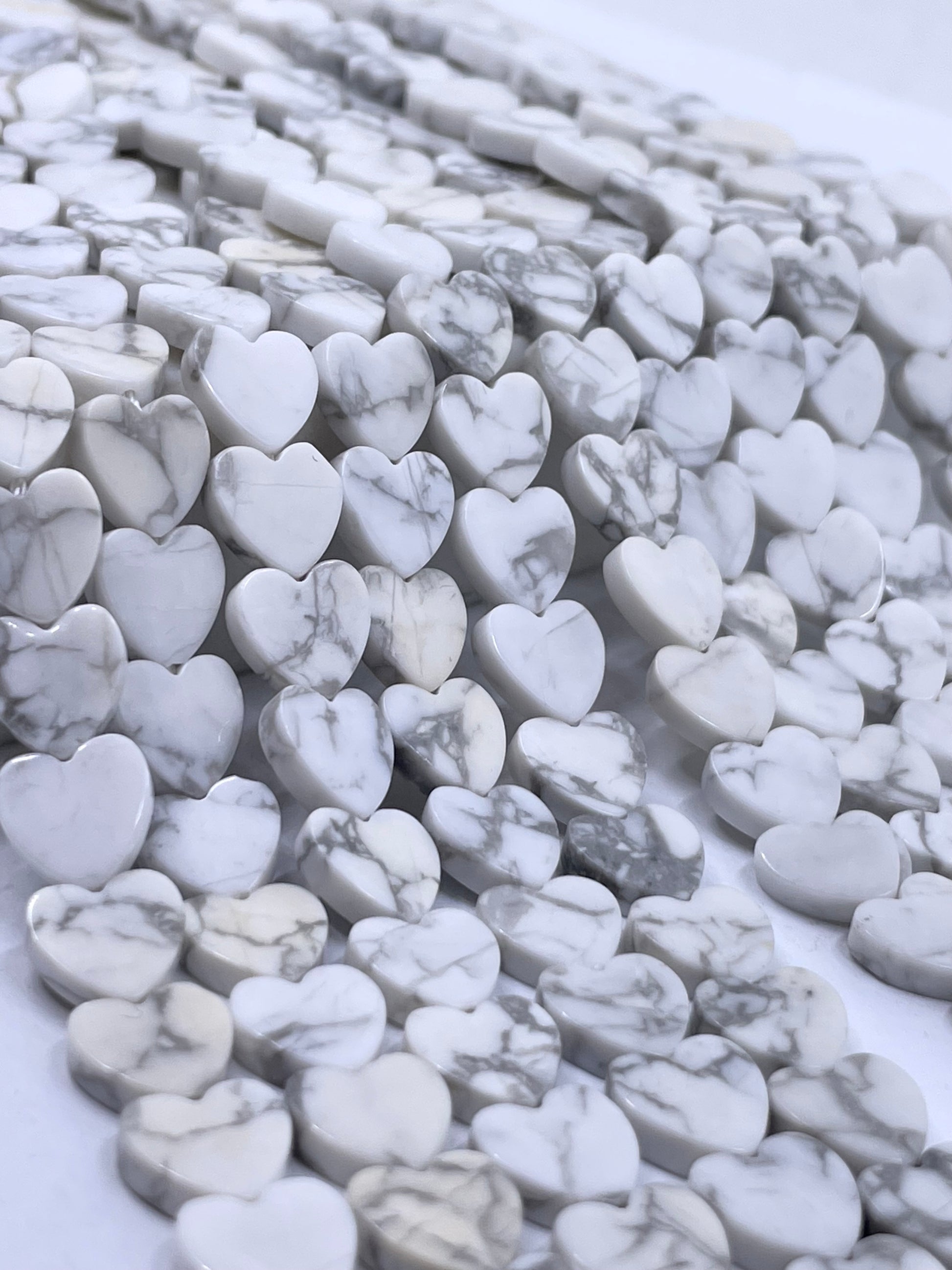 Heart-shaped white howlite beads with gray veining, arranged in rows on a white background.