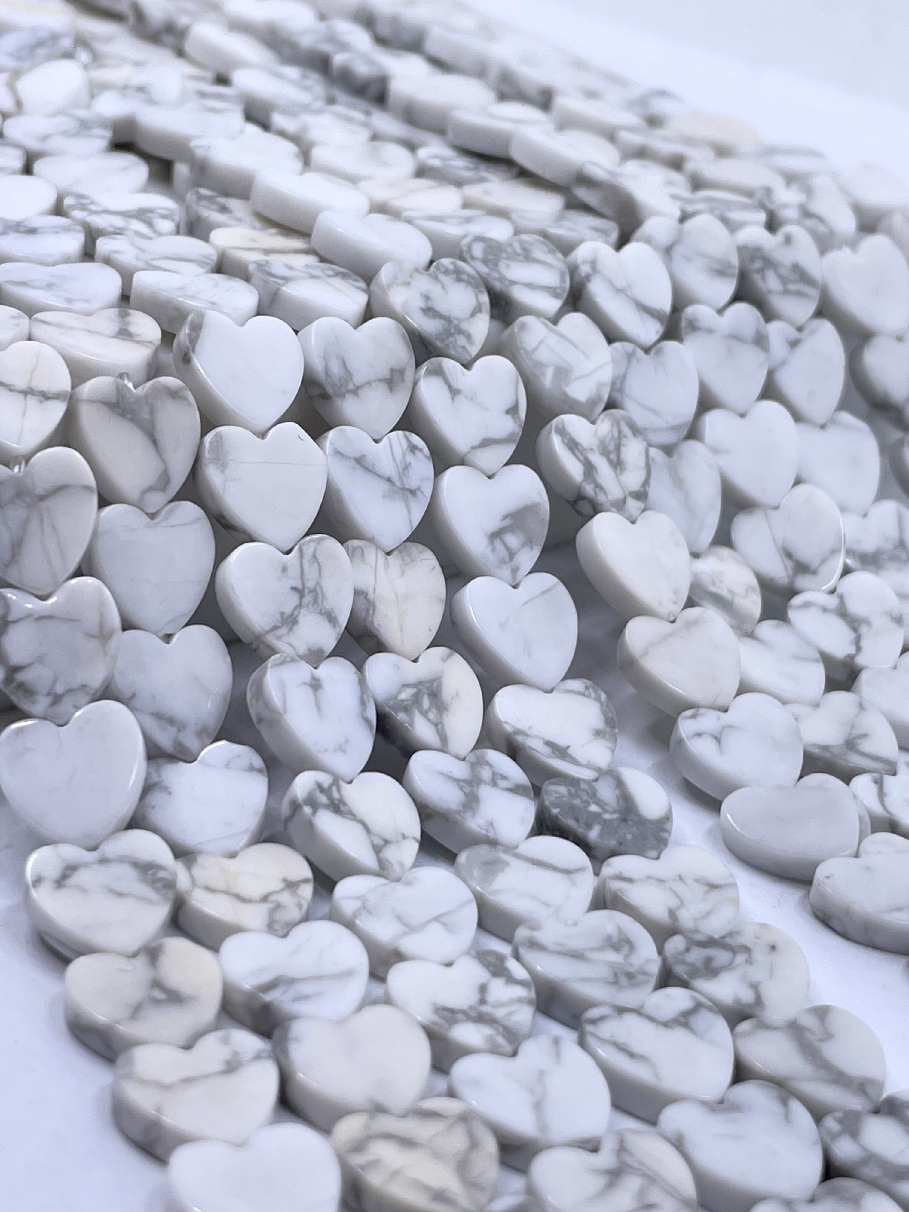 Heart-shaped white howlite beads with gray veining, arranged in rows on a white background.