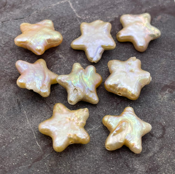 Nine iridescent star-shaped pearl beads arranged on a dark textured stone surface.
