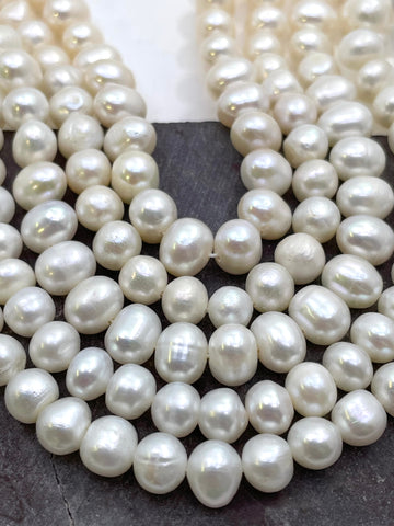 Close-up of multiple strands of irregular potato shape white freshwater pearls draped over a dark gray surface.