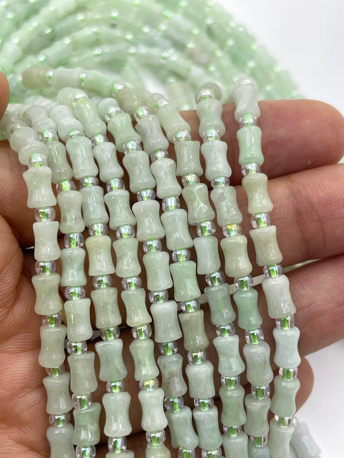 Green Burma Jade cylindrical beads with small silver spacer beads, held in a hand to show the strand length and texture.