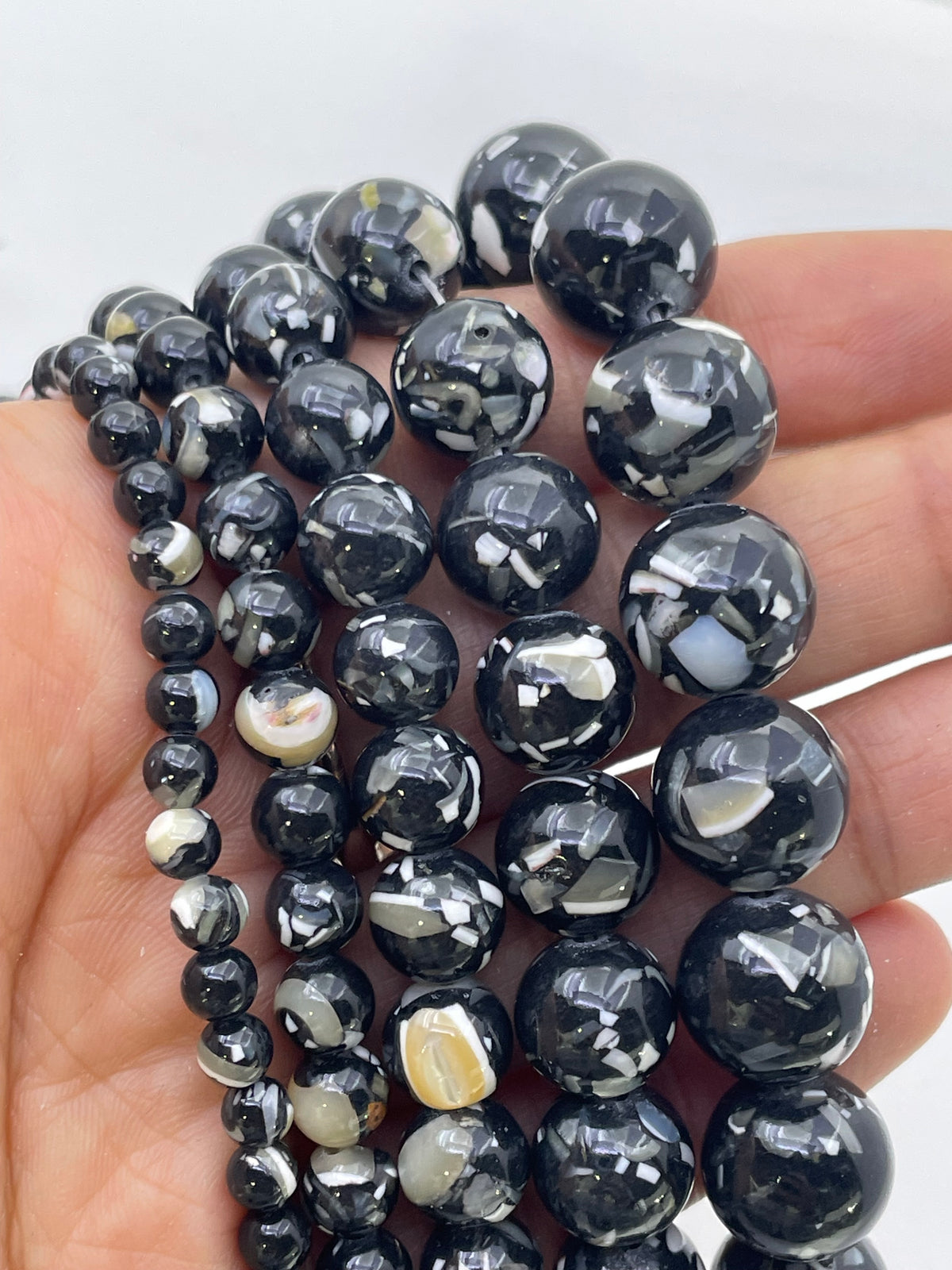 Black and white marbled mop beads strung on cords, held in a person's hand against a plain light background.