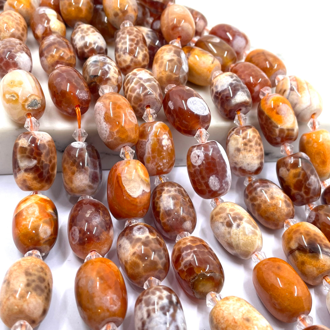 A close-up of polished agate stone beads with natural mottled patterns in shades of brown, orange, cream, and white, strung on clear cords.