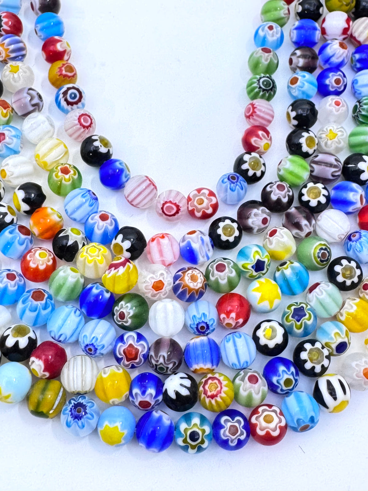 A close-up of a multi-strands of colorful glass beads with various patterns including floral, striped, and solid colors on a white background.