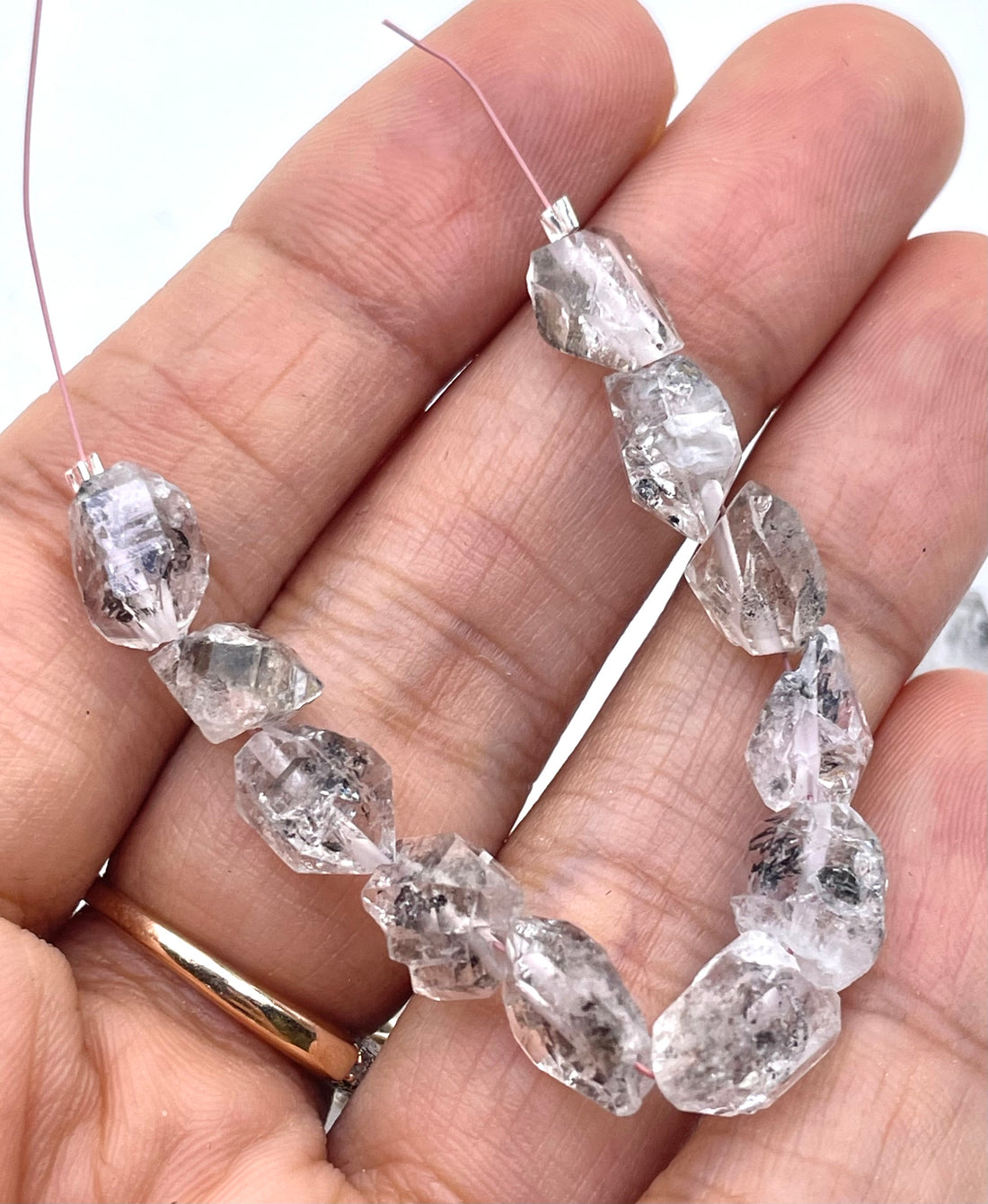 Rough clear herkimer diamond beads with visible inclusions and smoky gray tones, arranged on a white background.