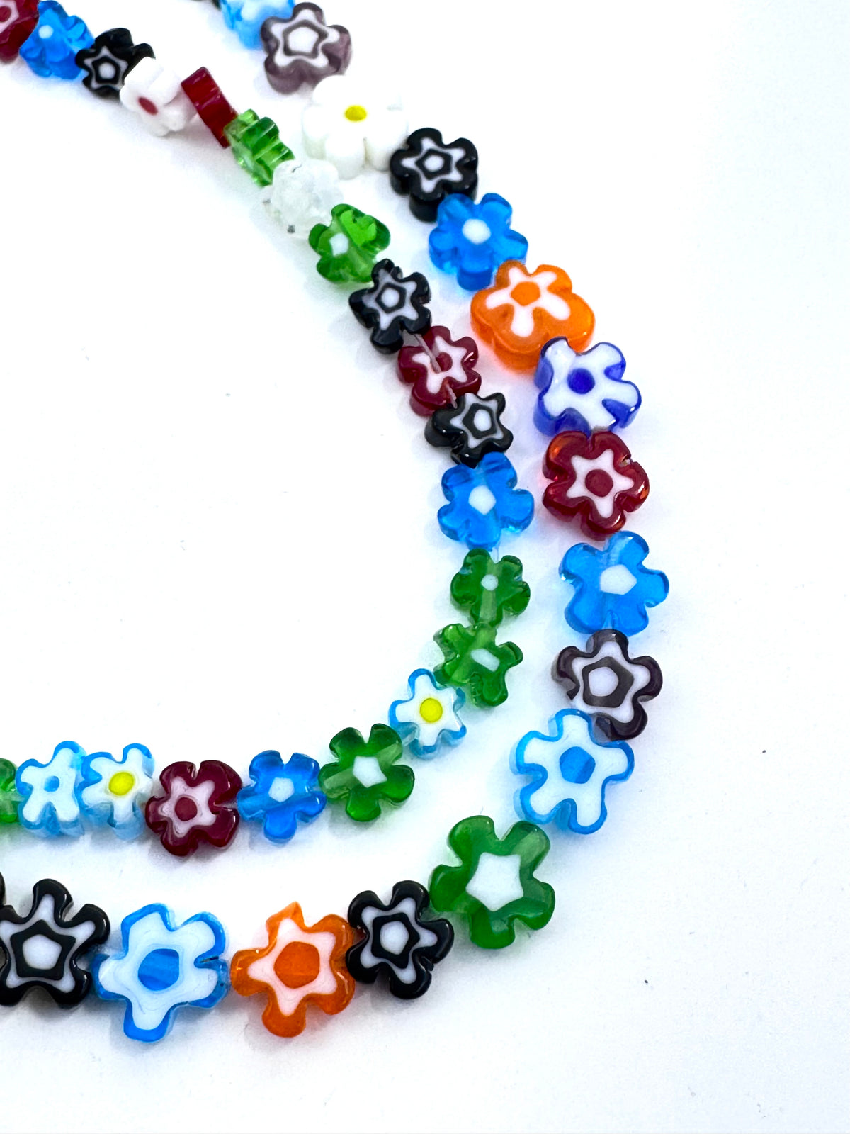 A close-up of a beaded strand featuring translucent, flower-shaped beads in multiple colors including blue, green, orange, red, black, white, and purple, arranged in a curved line on a plain white background.