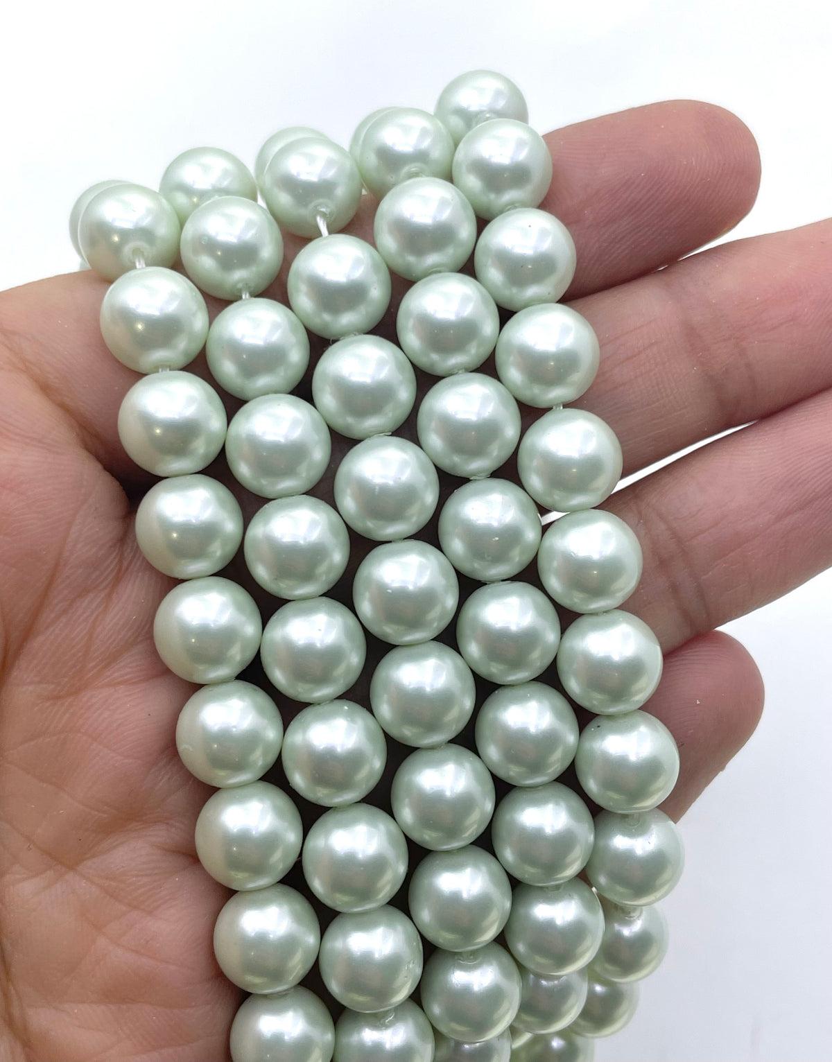A hand holding a strand of round, lustrous shell pearl beads in a pale mint green color against a plain white background.