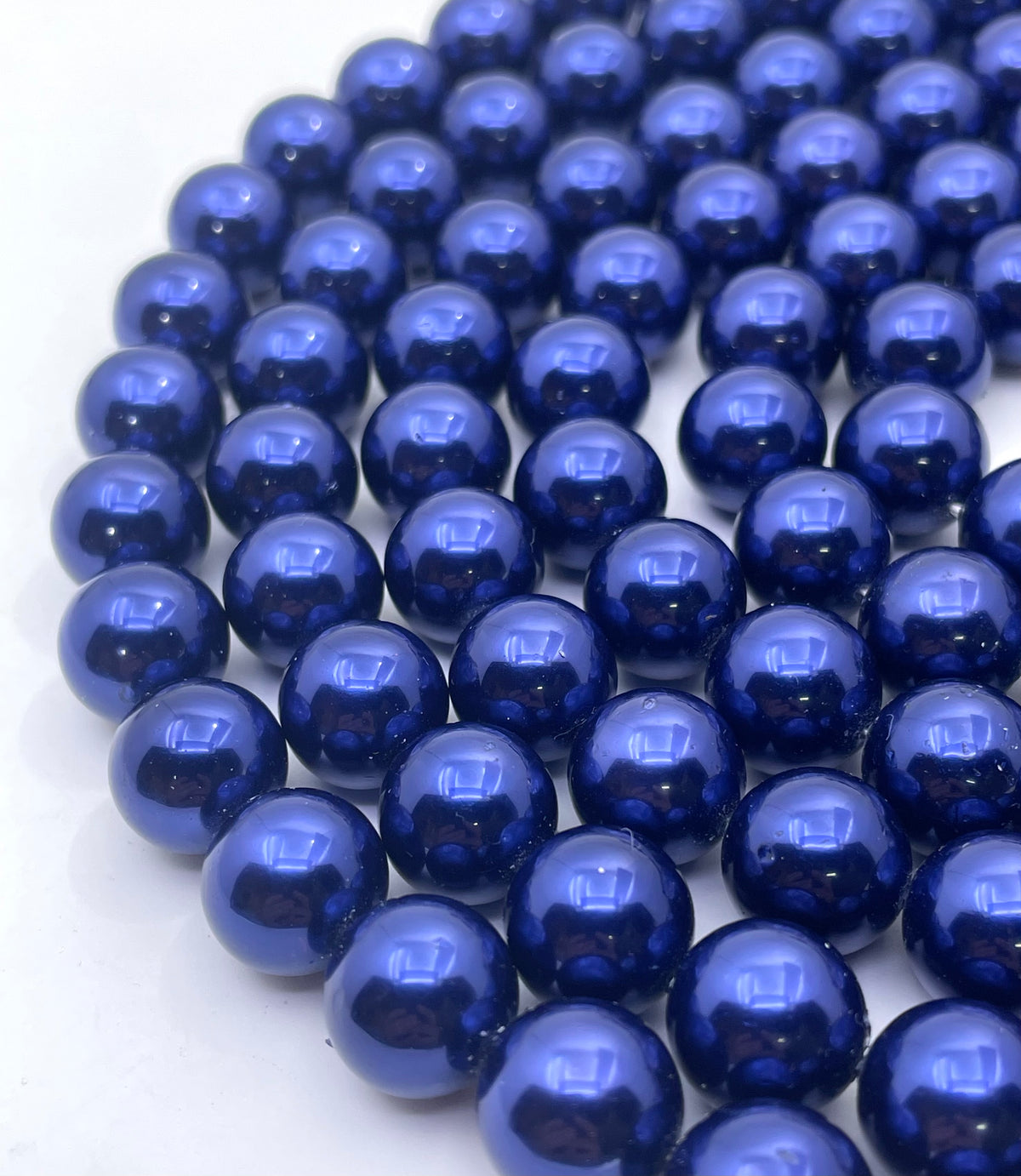 A close-up of glossy, metallic deep blue round shell pearl beads arranged in a curved line on a plain white background.