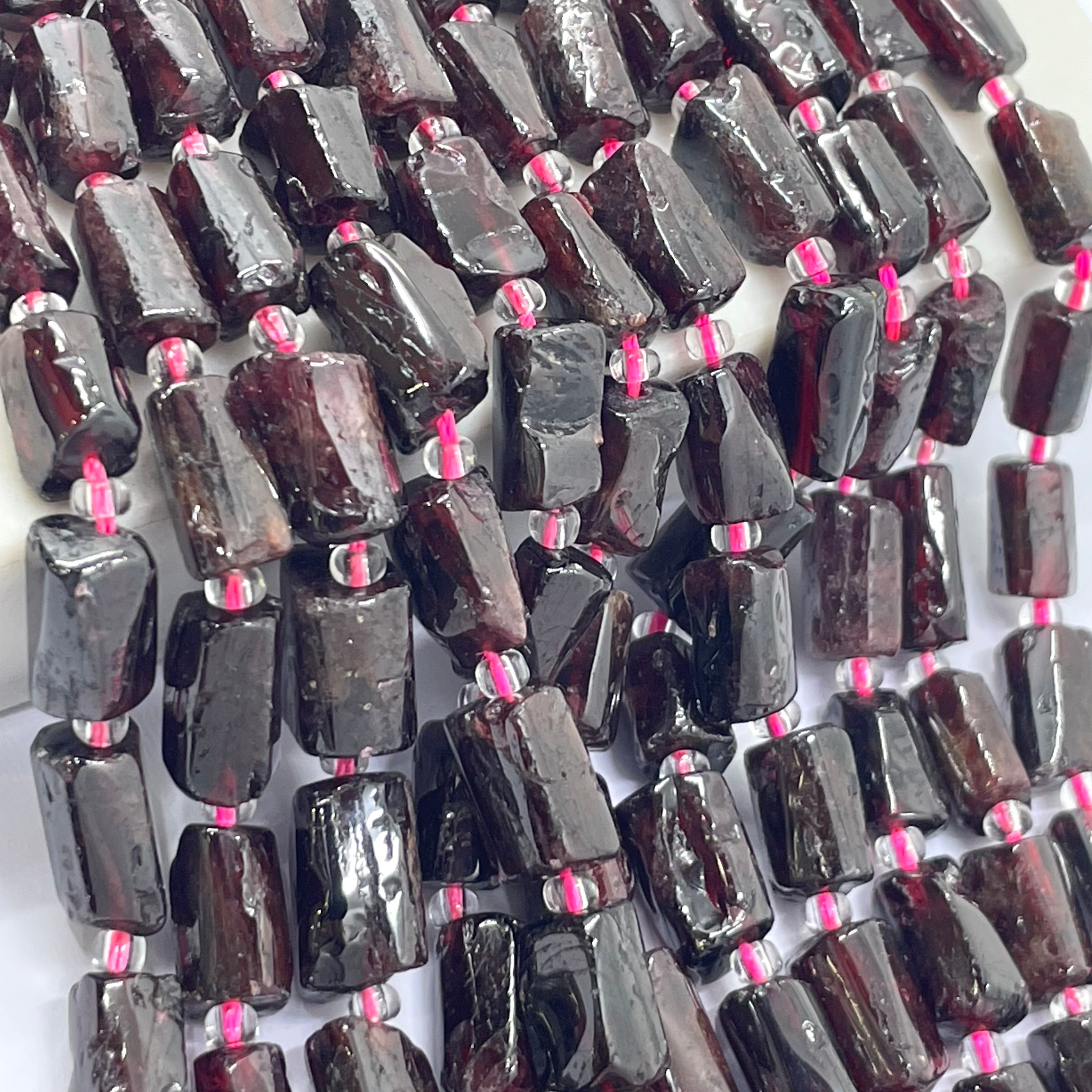 Dark reddish-brown polished garnet gemstone beads strung on a white cord, arranged in rows on a white background.