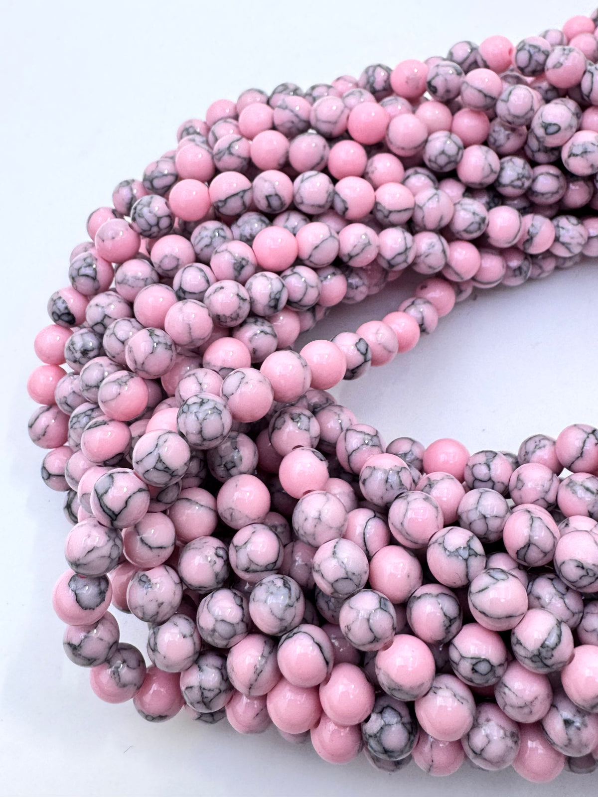 Multiple strands of round pink howlite gemstone beads with gray and white marbled veining, arranged on a plain white background.