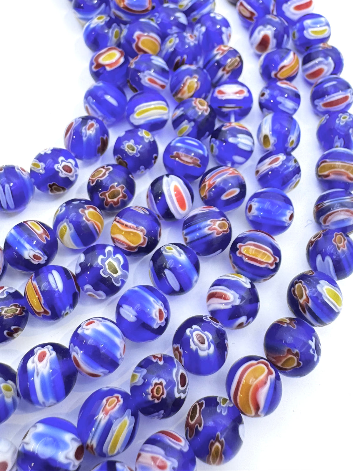 Multiple strands of round glass beads in a cobalt blue color, decorated with hand-painted patterns of white, yellow, orange, and red swirls and floral motifs, set against a plain white background.