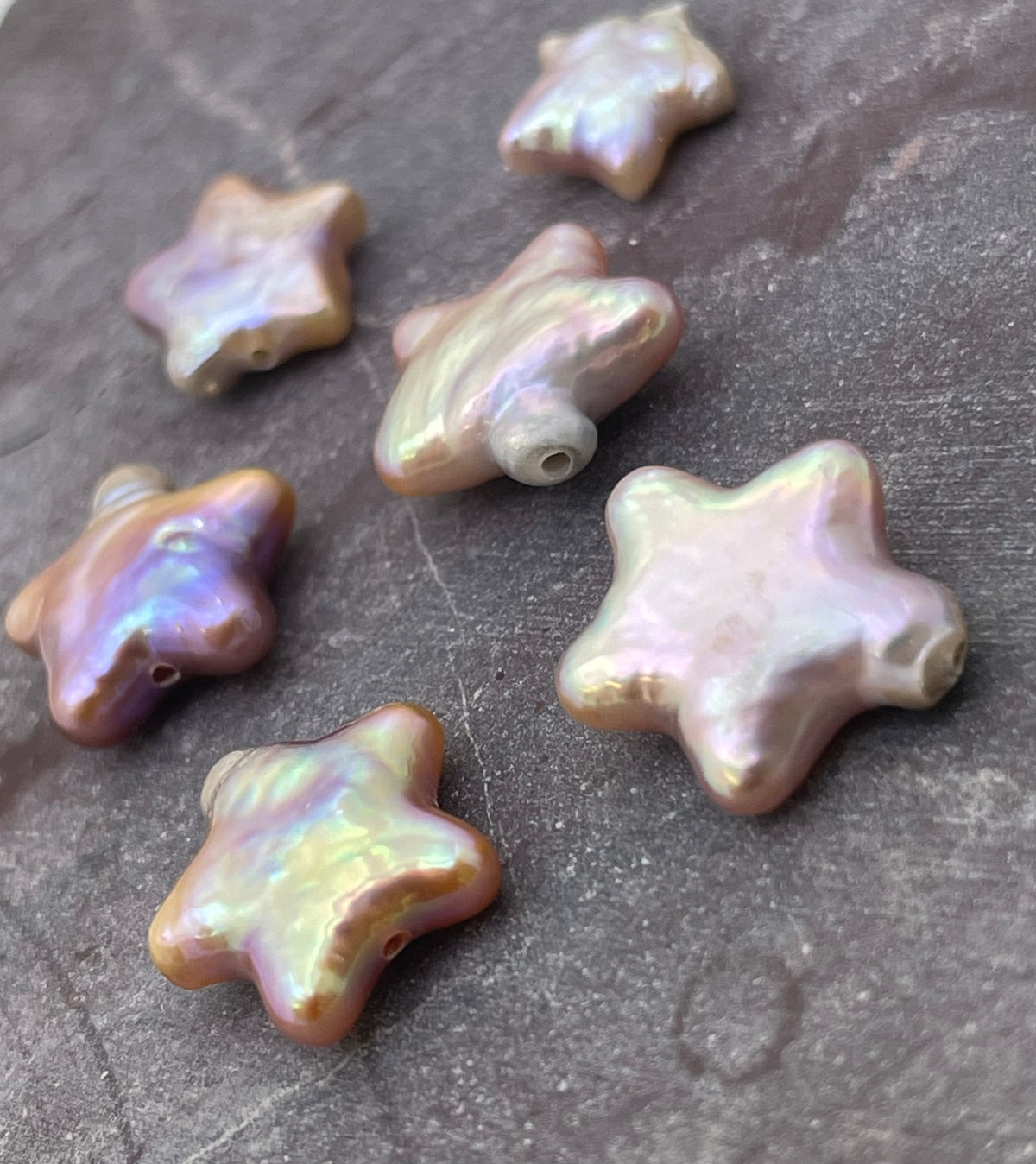 Six iridescent star-shaped baroque pearls arranged on a textured gray surface.
