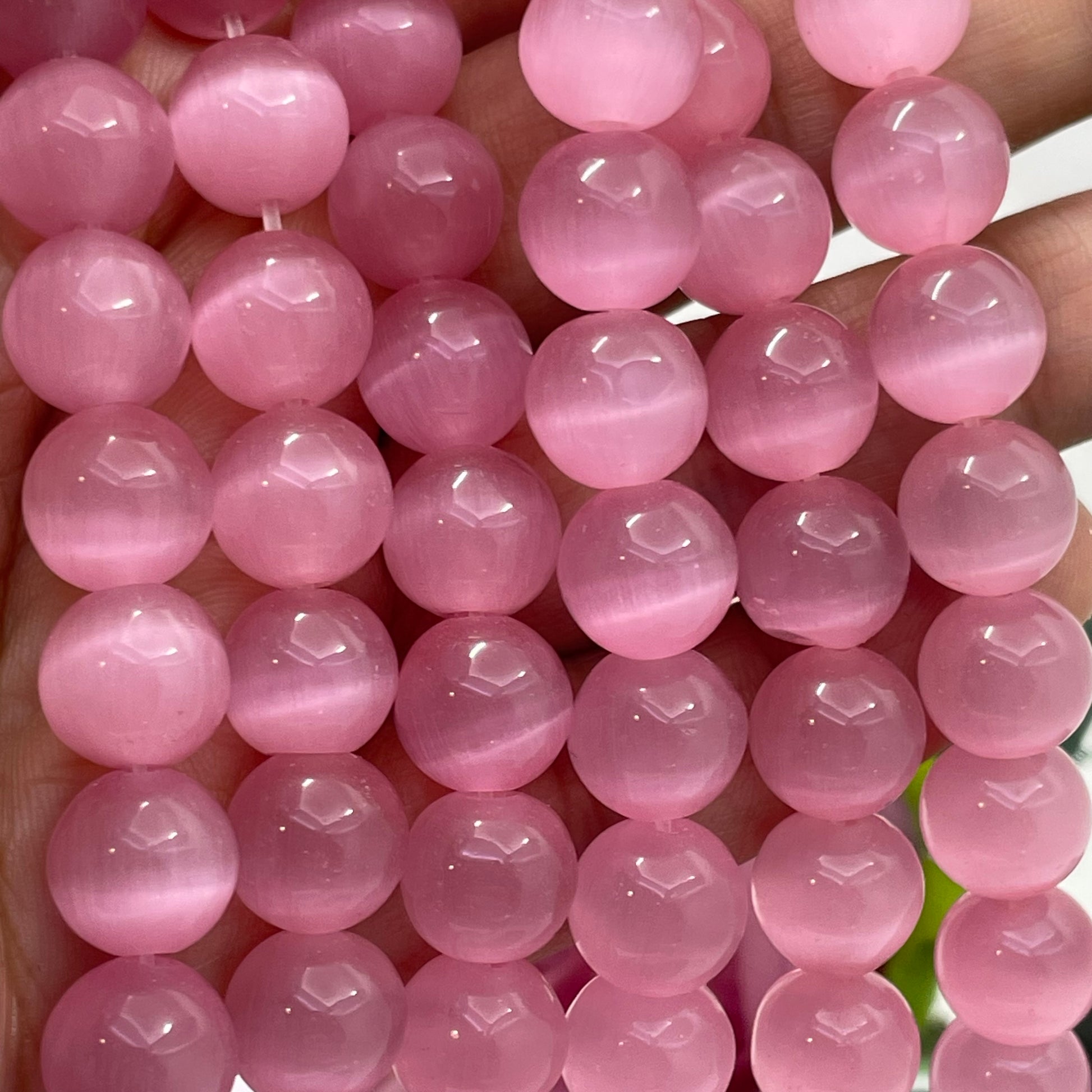 A close-up of pink cats eye round beads strung together, held in a hand to show scale and texture.