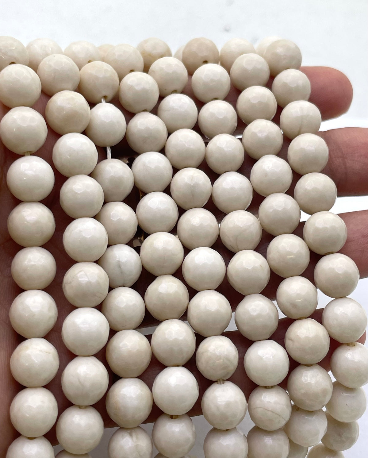 A close-up of many small round off-white fossil stone beads held in a hand against a plain light background.