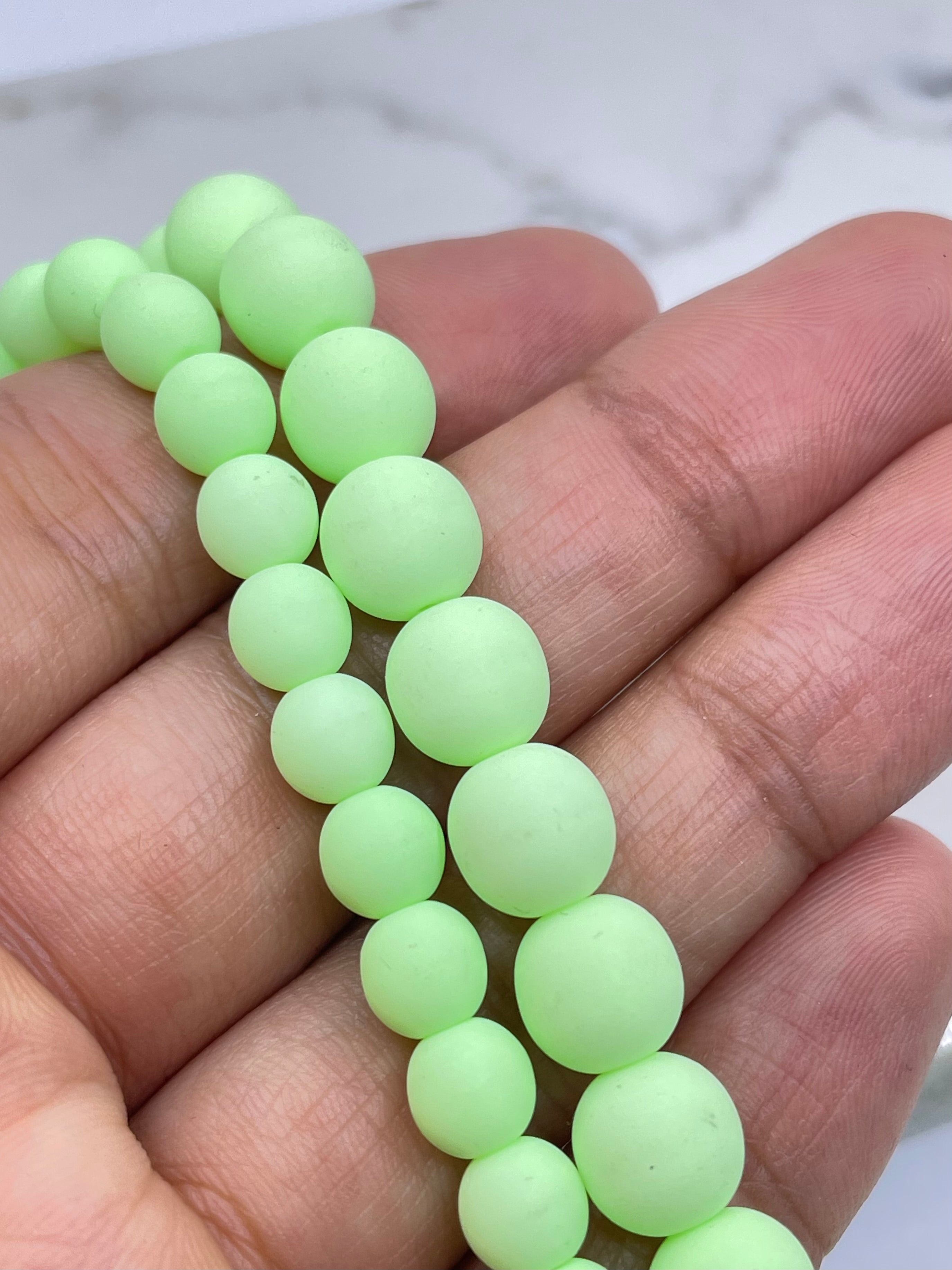 A close-up of a hand holding a strand of matte, pale neon yellow-green round beads.