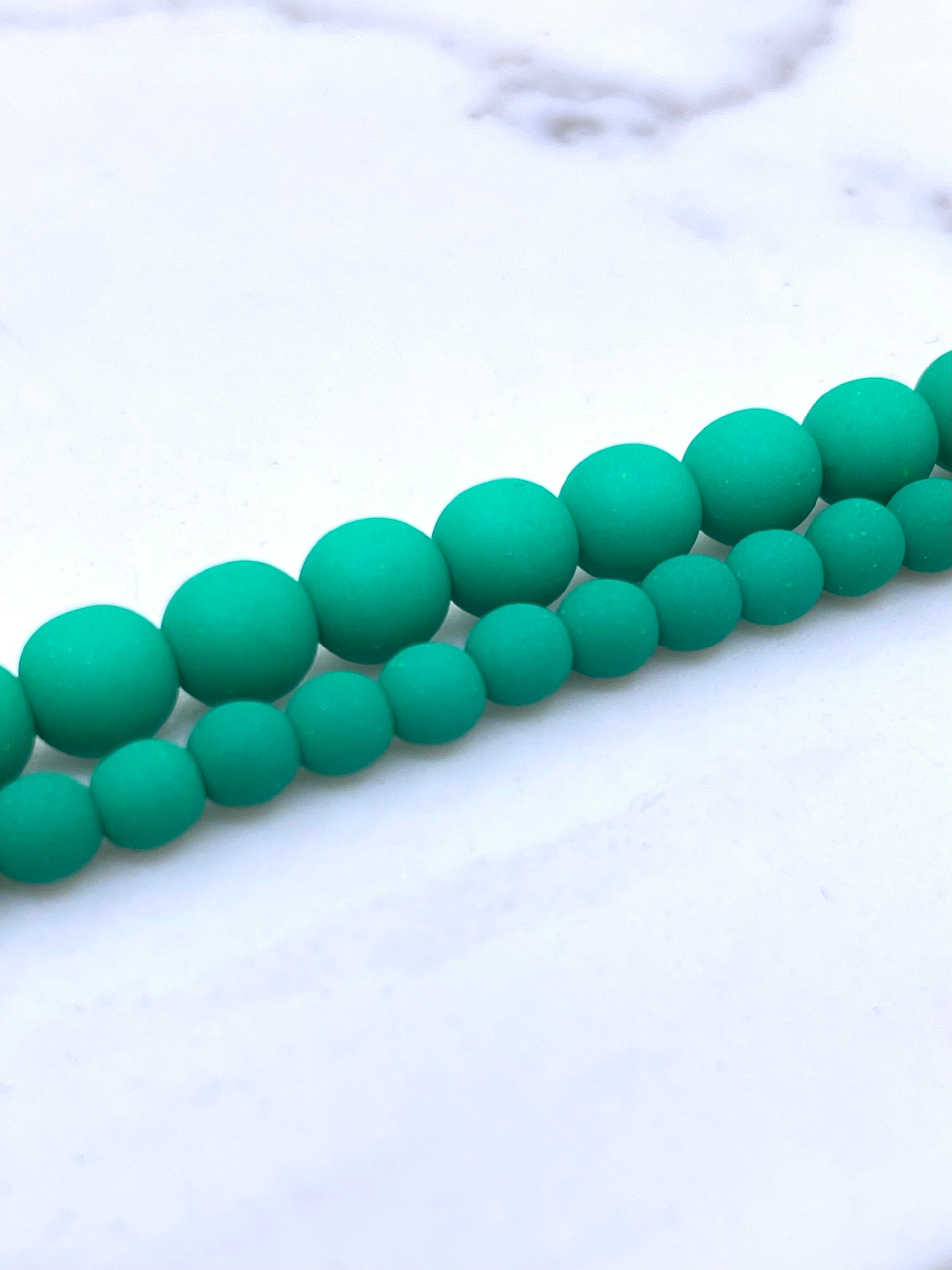 Green matte velvet round beads strung in two parallel rows on a white marble surface.