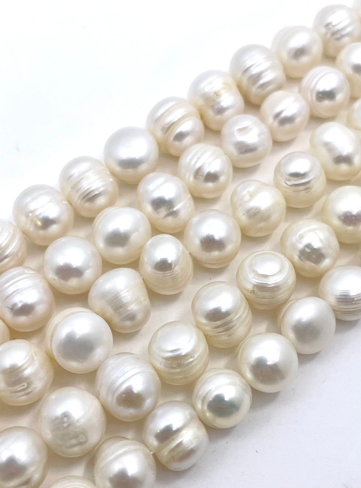 Close-up of strands of round, lustrous white pearl beads arranged diagonally on a plain white background.