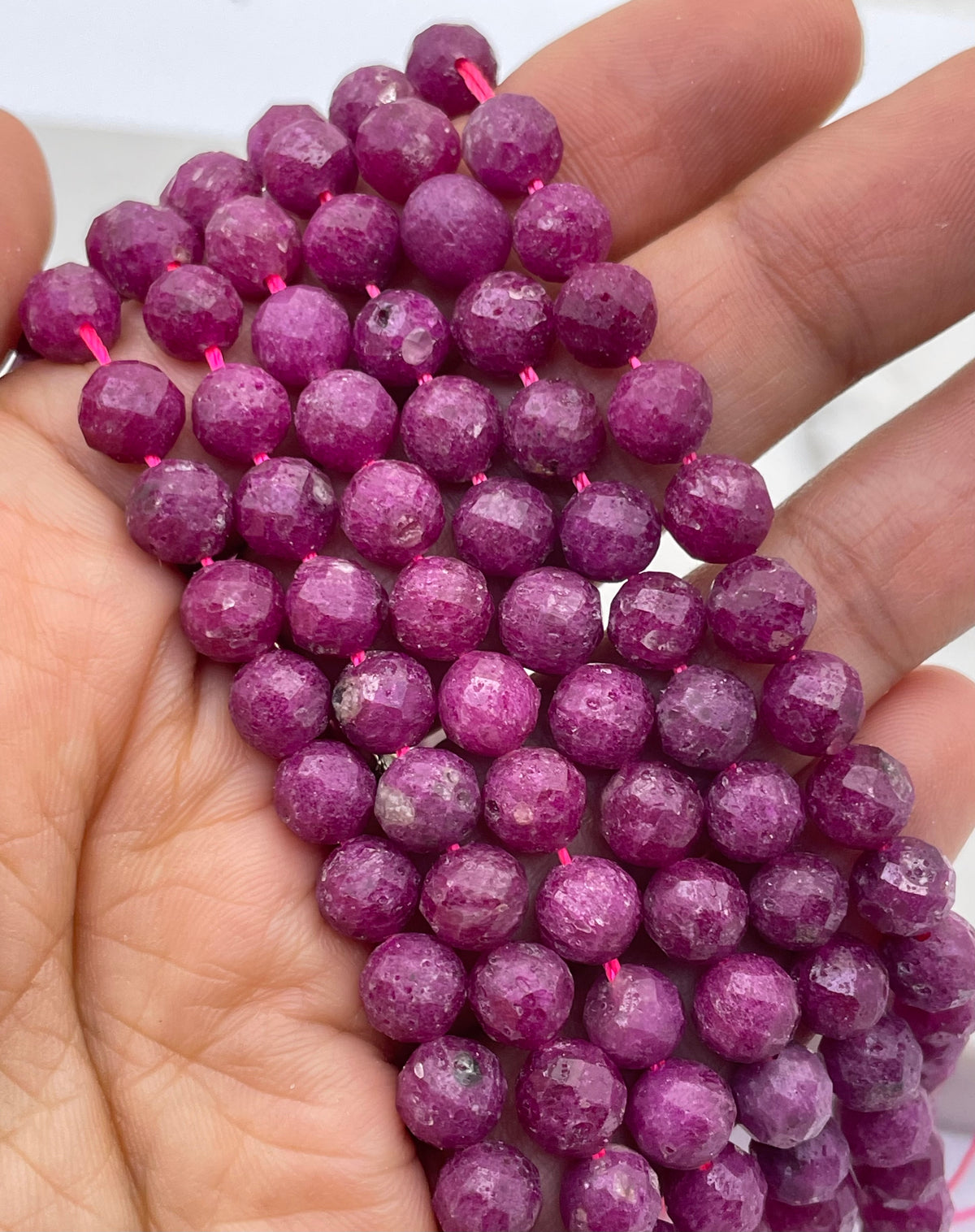 Faceted round ruby purple beads strung on a pink thread, held in a person's hand.