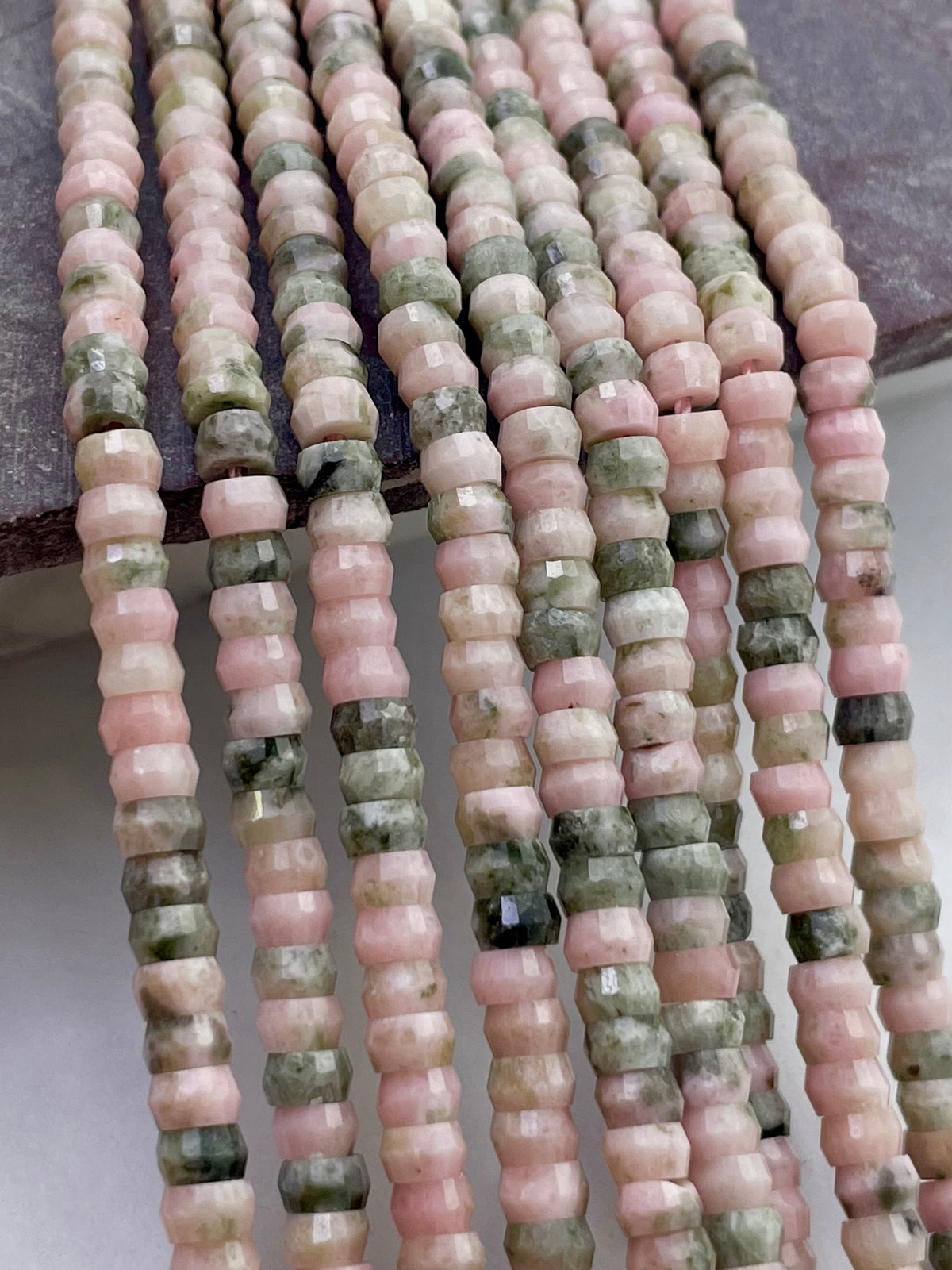 Faceted nevada lapis beads in alternating pink and green stone strands draped over a dark surface.