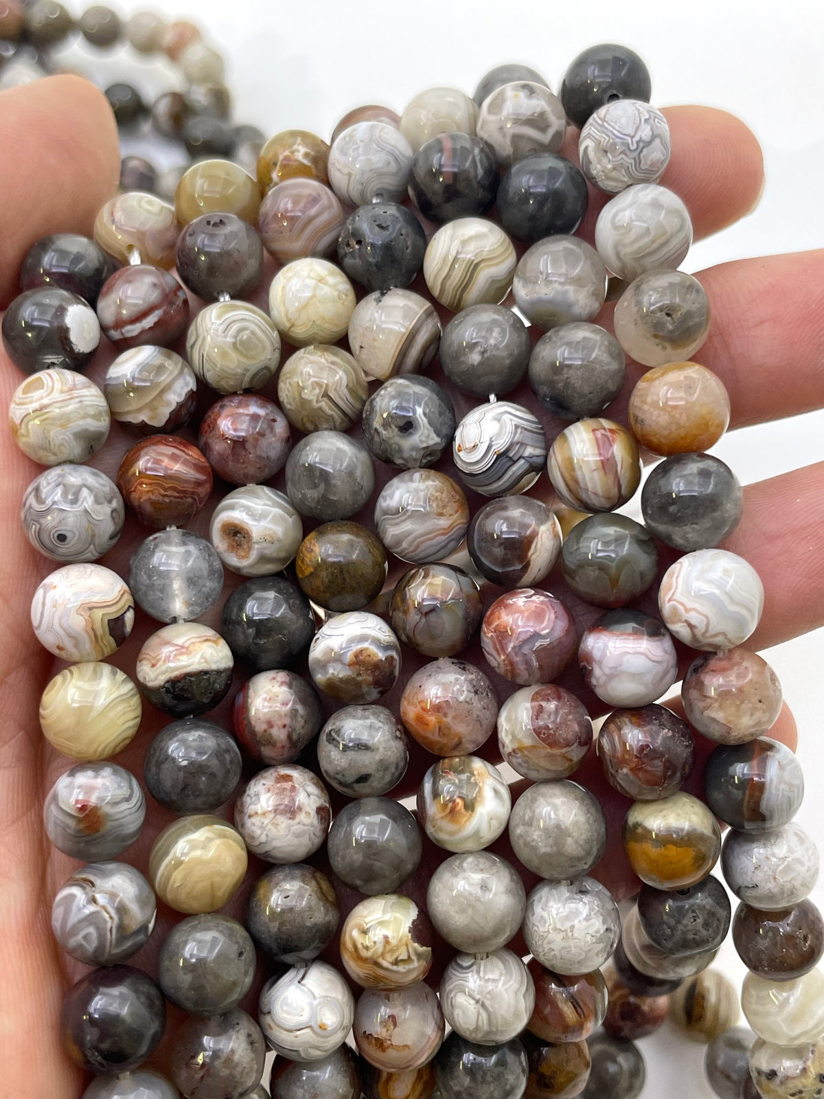 A close-up of a hand holding a strand of round agate stone beads with natural banding patterns in gray, white, brown, and black.
