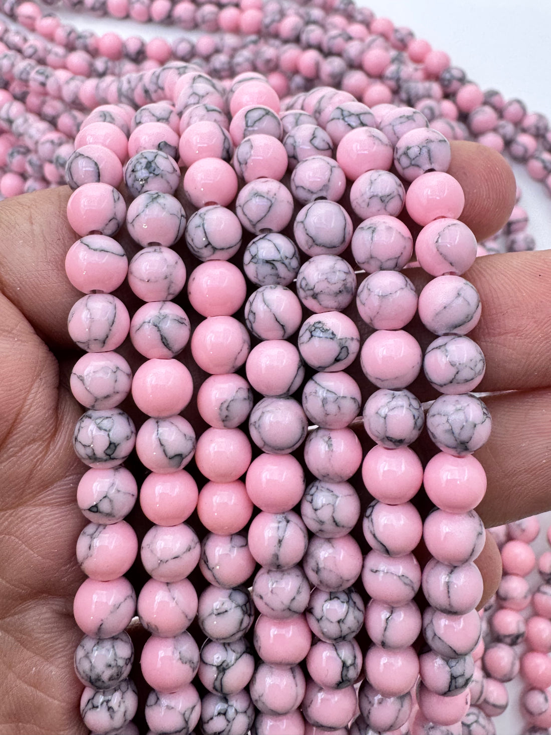 Multiple strands of round pink howlite gemstone beads with black and gray marbled veining, arranged in a layered display on a white background.