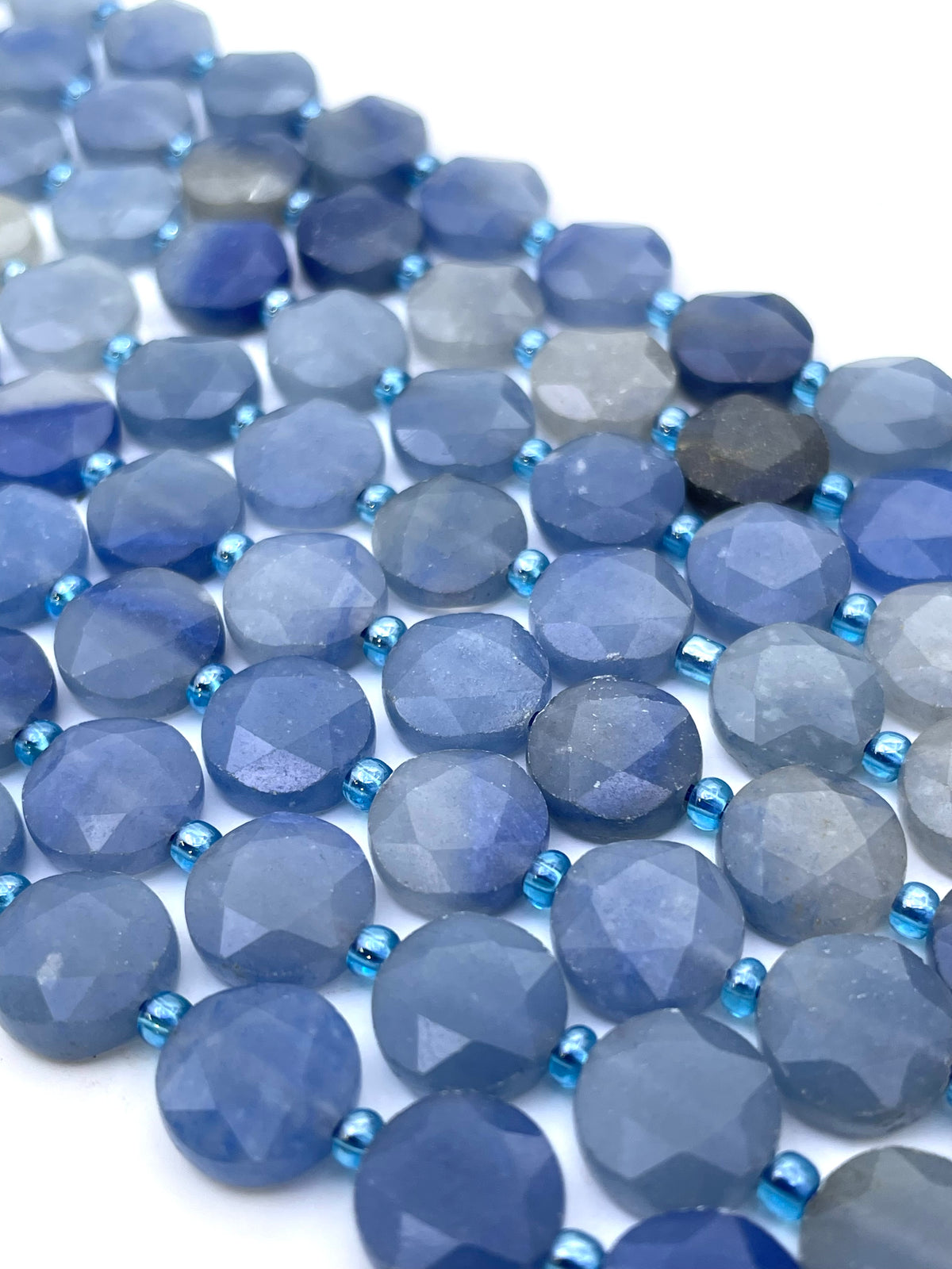 Faceted round blue aventurine beads in shades of blue and gray, separated by small metallic blue spacer beads, arranged on a white background.