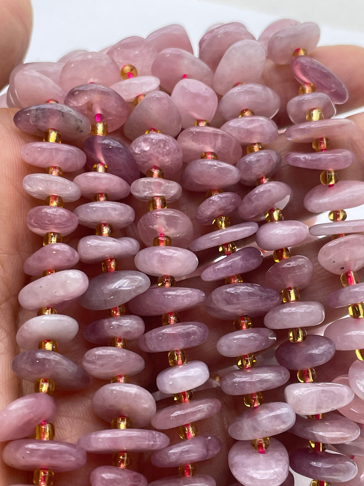 A close-up of multiple strands of pink Madagascar rose quartz beads threaded with small gold spacer beads, held in a hand against a plain light background.